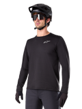 Alpinestars A-Dura Thermal Jersey, schwarzes Langarm-Mountainbike-Trikot, weißes Brust-Logo, getragen mit schwarzem Helm und Handschuhen, schlichtes sportliches Design für Trail-Fahrten