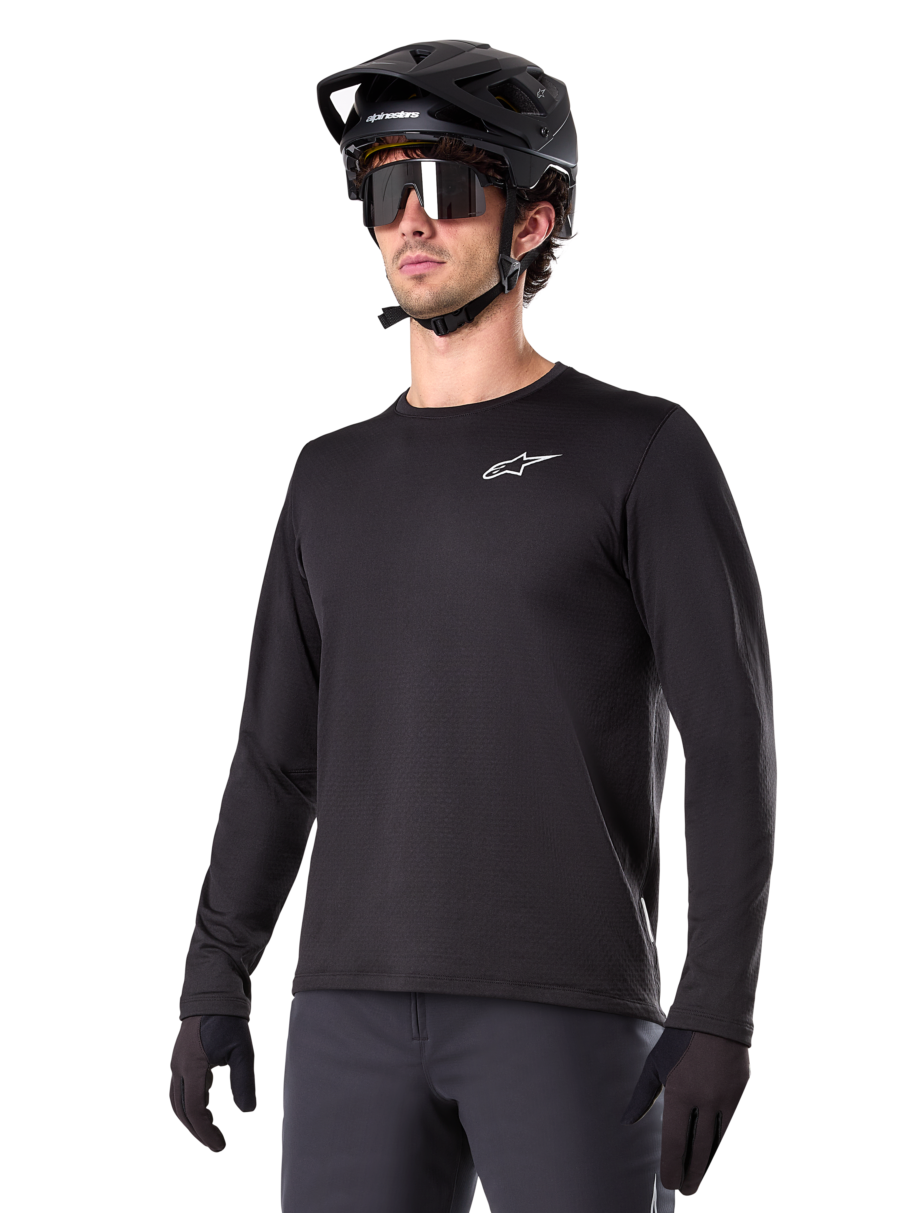 Alpinestars A-Dura Thermal Jersey, schwarzes Langarm-Mountainbike-Trikot, weißes Brust-Logo, getragen mit schwarzem Helm und Handschuhen, schlichtes sportliches Design für Trail-Fahrten