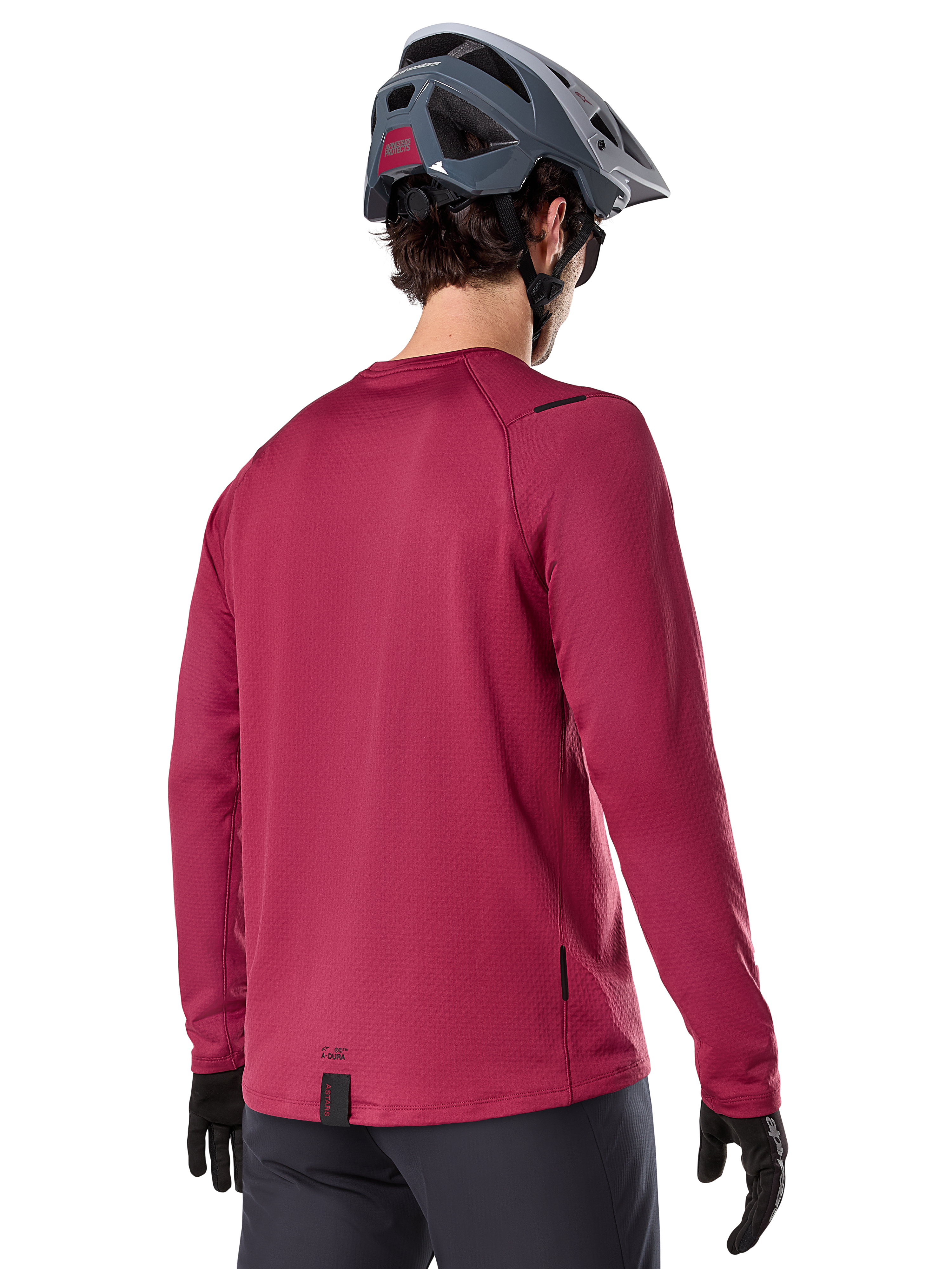 Alpinestars A-Dura Thermal Trikot, Langarm-Mountainbike-Trikot, Burgund, Rückansicht am Model mit grauem MTB-Helm und schwarzen Handschuhen, mit verlängertem Rückenteil und kleinen Logo-Details, entwickelt für Trail-Fahrten bei kaltem Wetter.