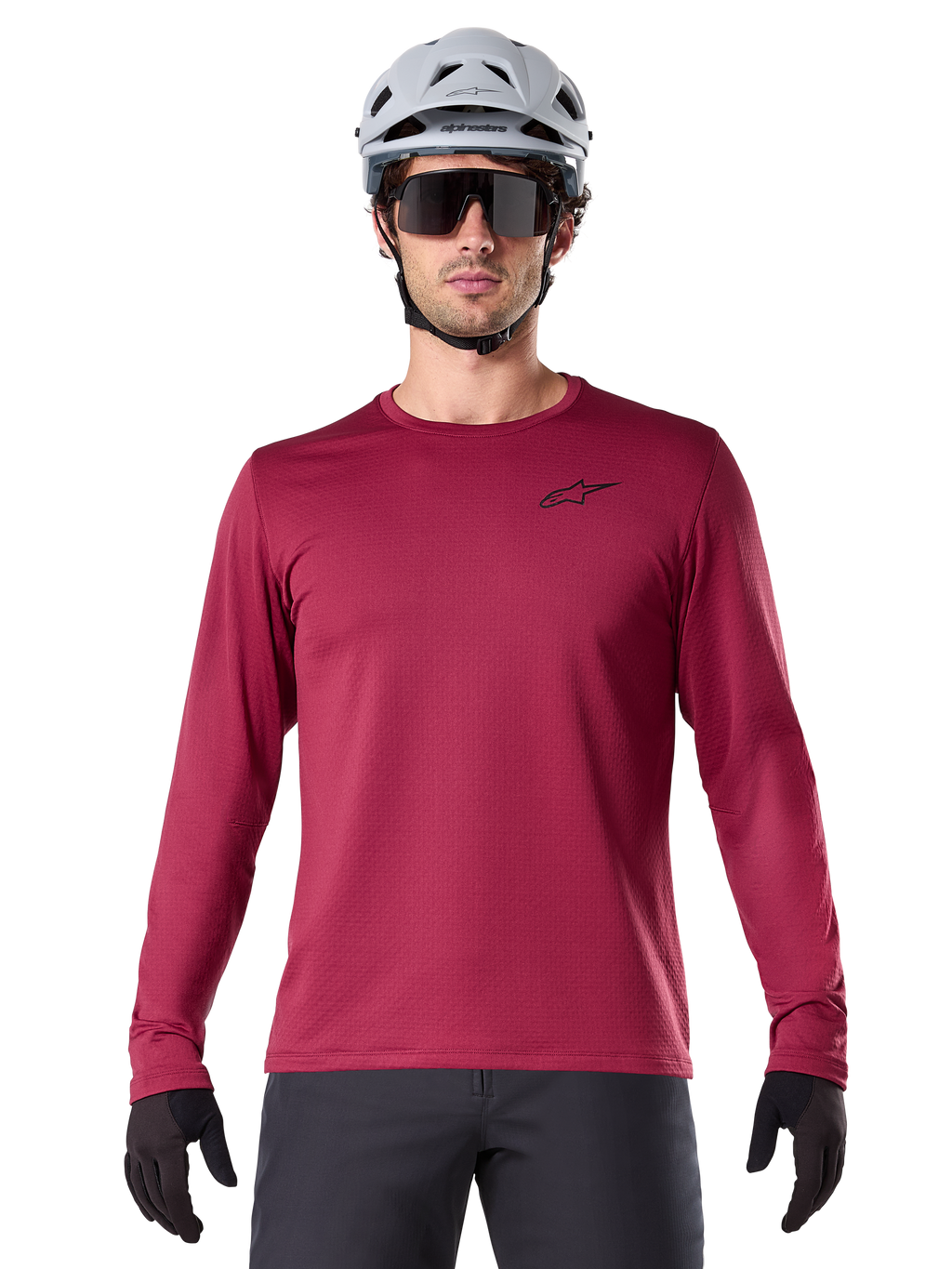 Männlicher Radfahrer trägt das Alpinestars A-Dura Thermal Jersey, langärmeliges MTB-Trikot, Burgunderrot, kombiniert mit einem grauen Helm und einer schwarzen Sonnenbrille, kleines schwarzes Stern-Logo auf der Brust, isoliertes Fleece-Material für Mountainbiking bei kaltem Wetter