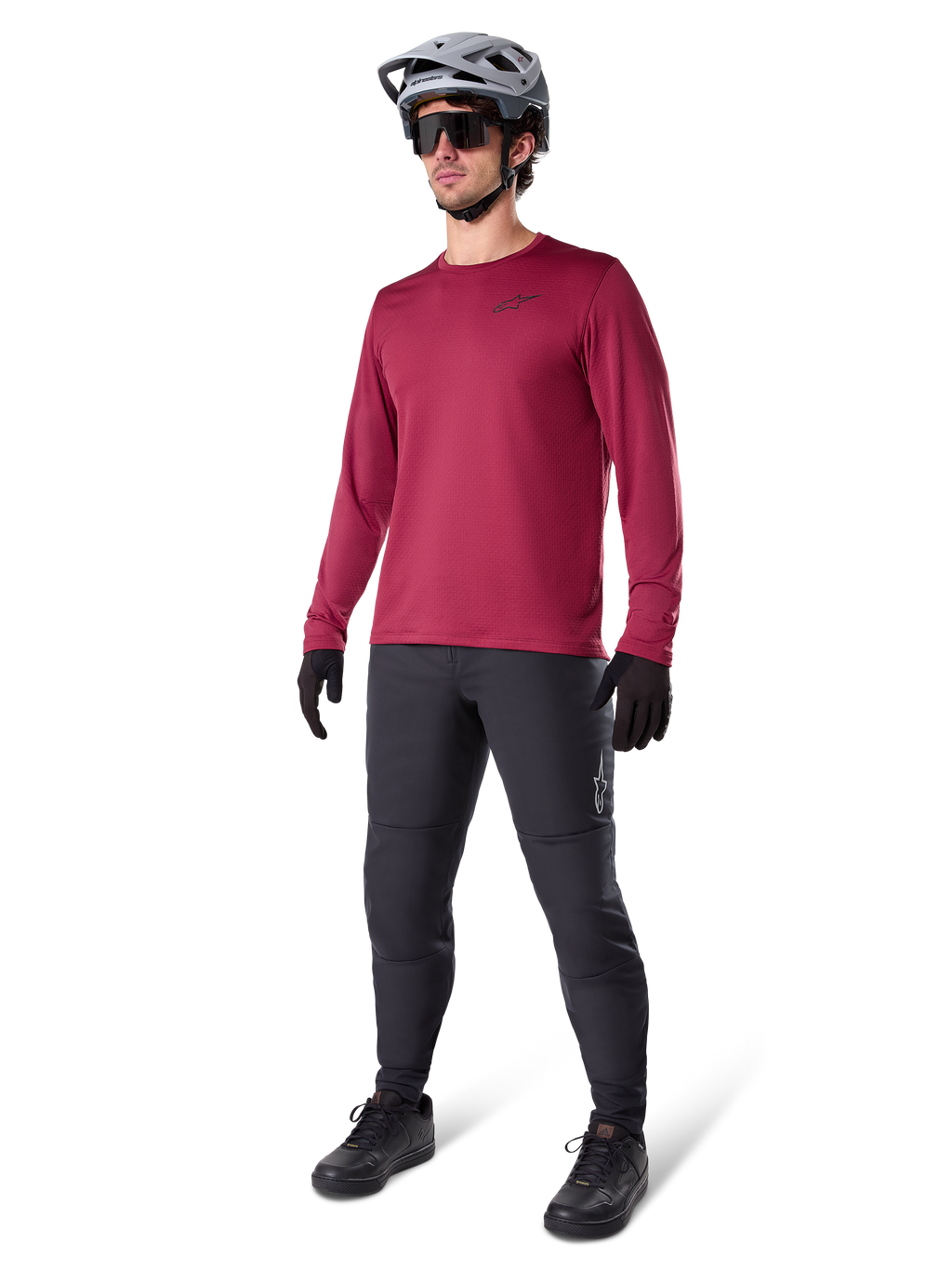 Alpinestars A-Dura Thermal Jersey in Burgundy, langärmliges, isoliertes Radsport-Oberteil getragen mit dunkelgrauer Mountainbike-Hose, schwarzen Handschuhen und einem grauen Helm, Ganzkörper-Studioaufnahme von Kaltwetter-MTB-Ausrüstung.