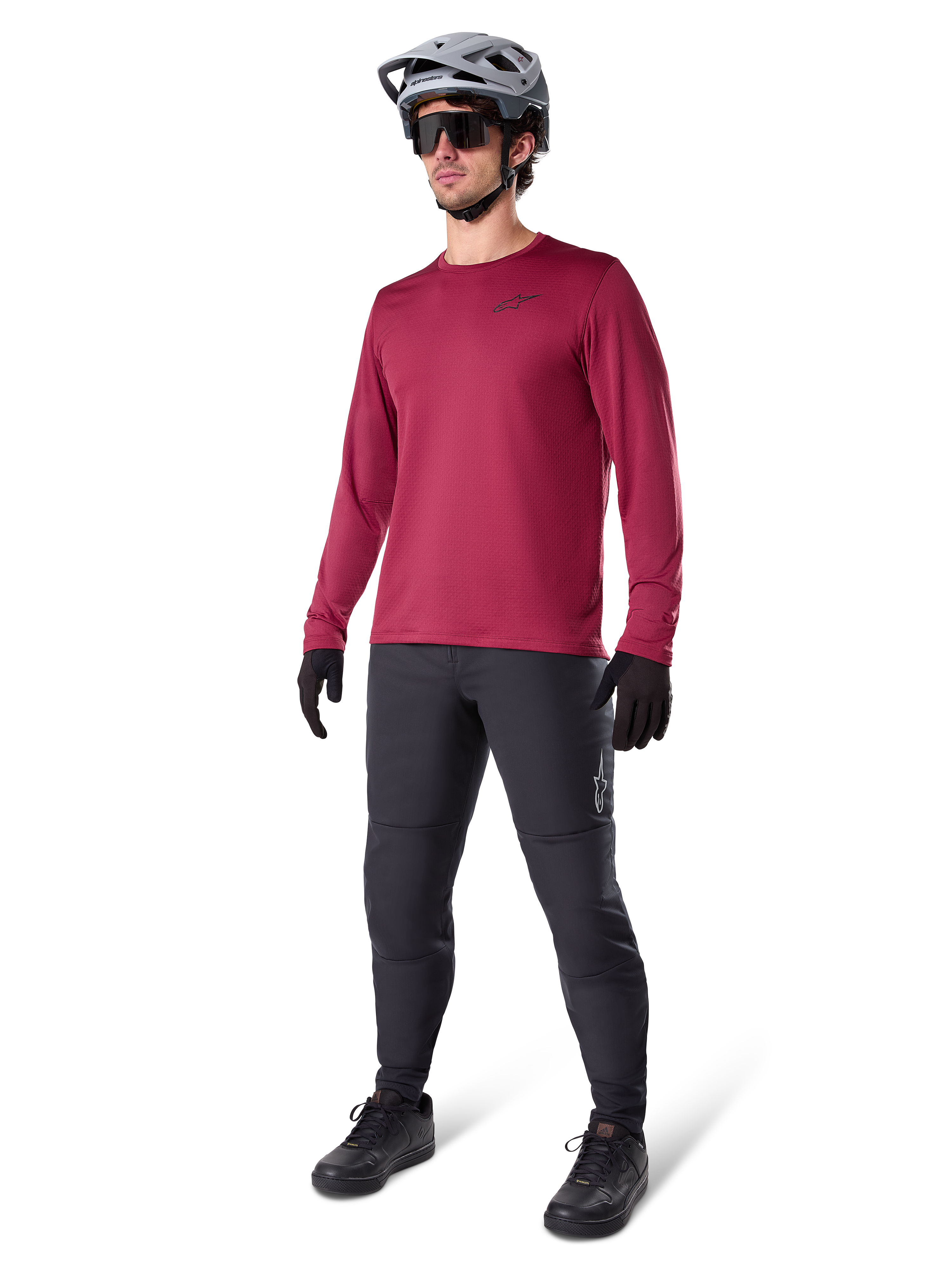 Alpinestars A-Dura Thermal Jersey in Burgundy, langärmliges, isoliertes Radsport-Oberteil getragen mit dunkelgrauer Mountainbike-Hose, schwarzen Handschuhen und einem grauen Helm, Ganzkörper-Studioaufnahme von Kaltwetter-MTB-Ausrüstung.