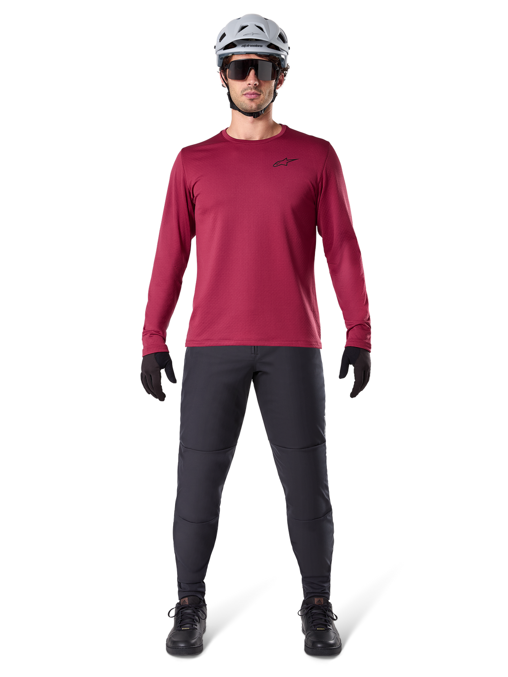 Männliches Model im Alpinestars A-Dura Thermal Jersey in Burgundy, langärmeliges isoliertes Radsport-Oberteil, kombiniert mit dunkelgrauer Mountainbike-Hose, weißem Helm, schwarzer Sonnenbrille und schwarzen Handschuhen, professionelle MTB-Ausrüstung für kaltes Wetter
