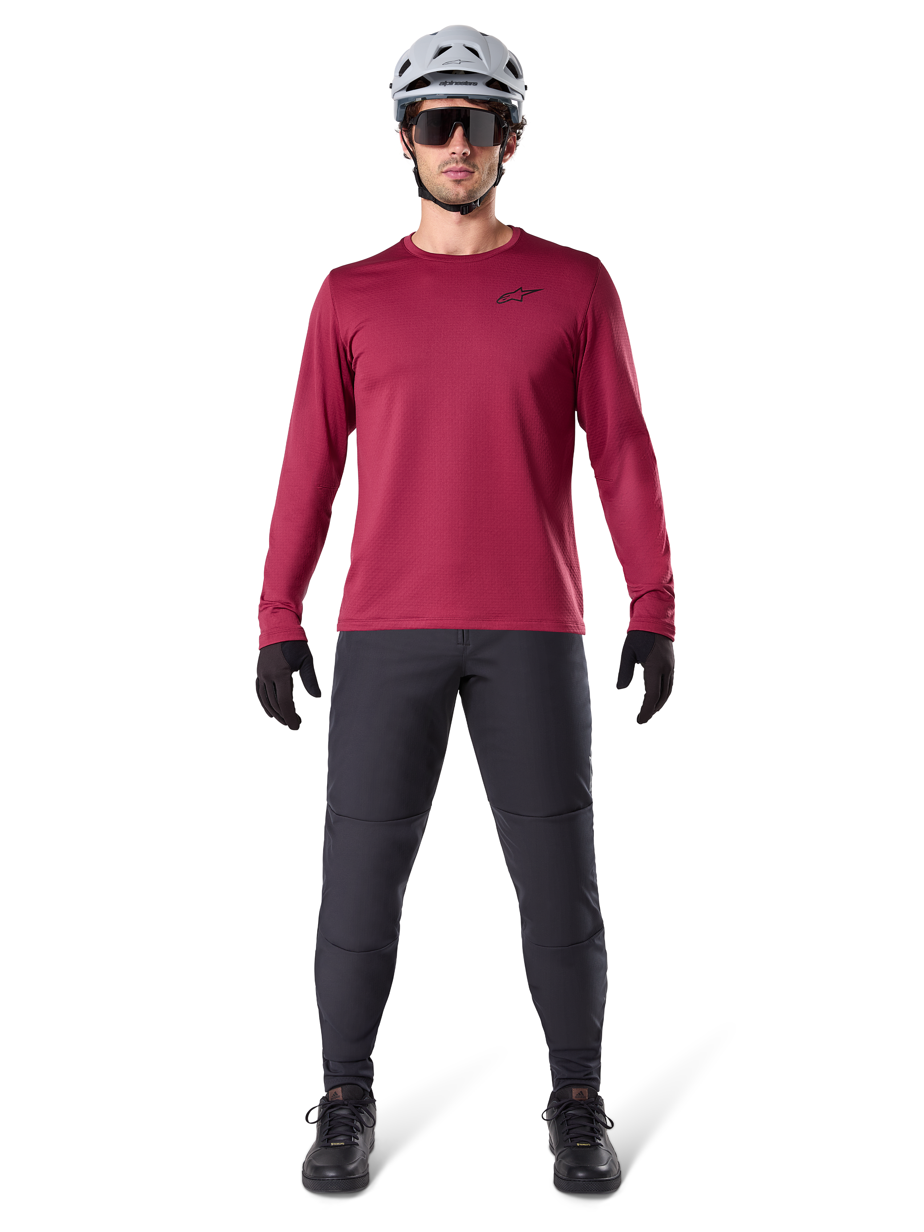 Männliches Model im Alpinestars A-Dura Thermal Jersey in Burgundy, langärmeliges isoliertes Radsport-Oberteil, kombiniert mit dunkelgrauer Mountainbike-Hose, weißem Helm, schwarzer Sonnenbrille und schwarzen Handschuhen, professionelle MTB-Ausrüstung für kaltes Wetter