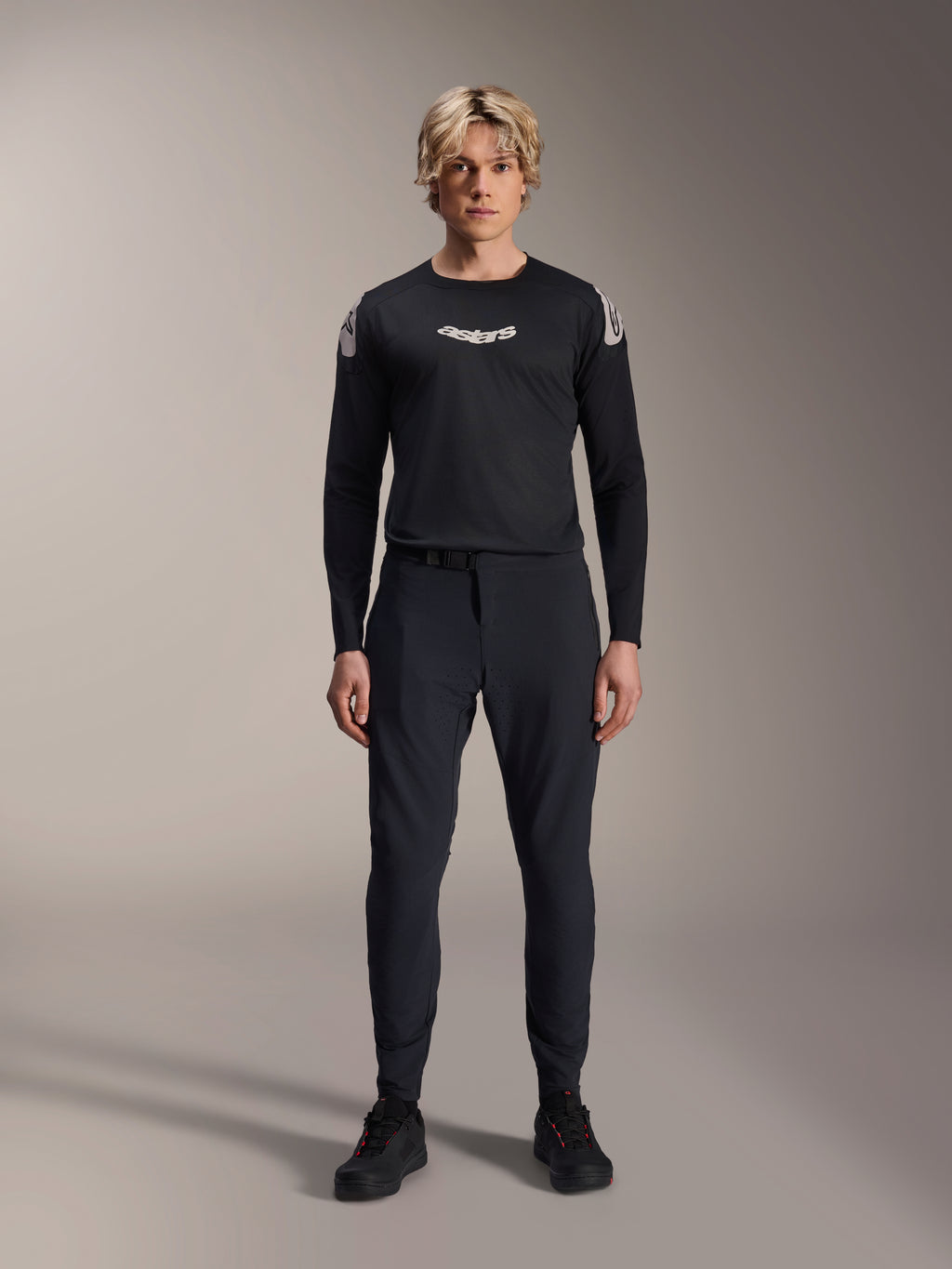 Alpinestars A-Aria Elite Hose, MTB-Hose in Black Titanium, getragen von einem männlichen Model mit einem passenden schwarzen Langarm-Trikot und Sneakern, Slim-Fit Performance-Design mit Magnetverschluss, technische Mountainbike-Bekleidung