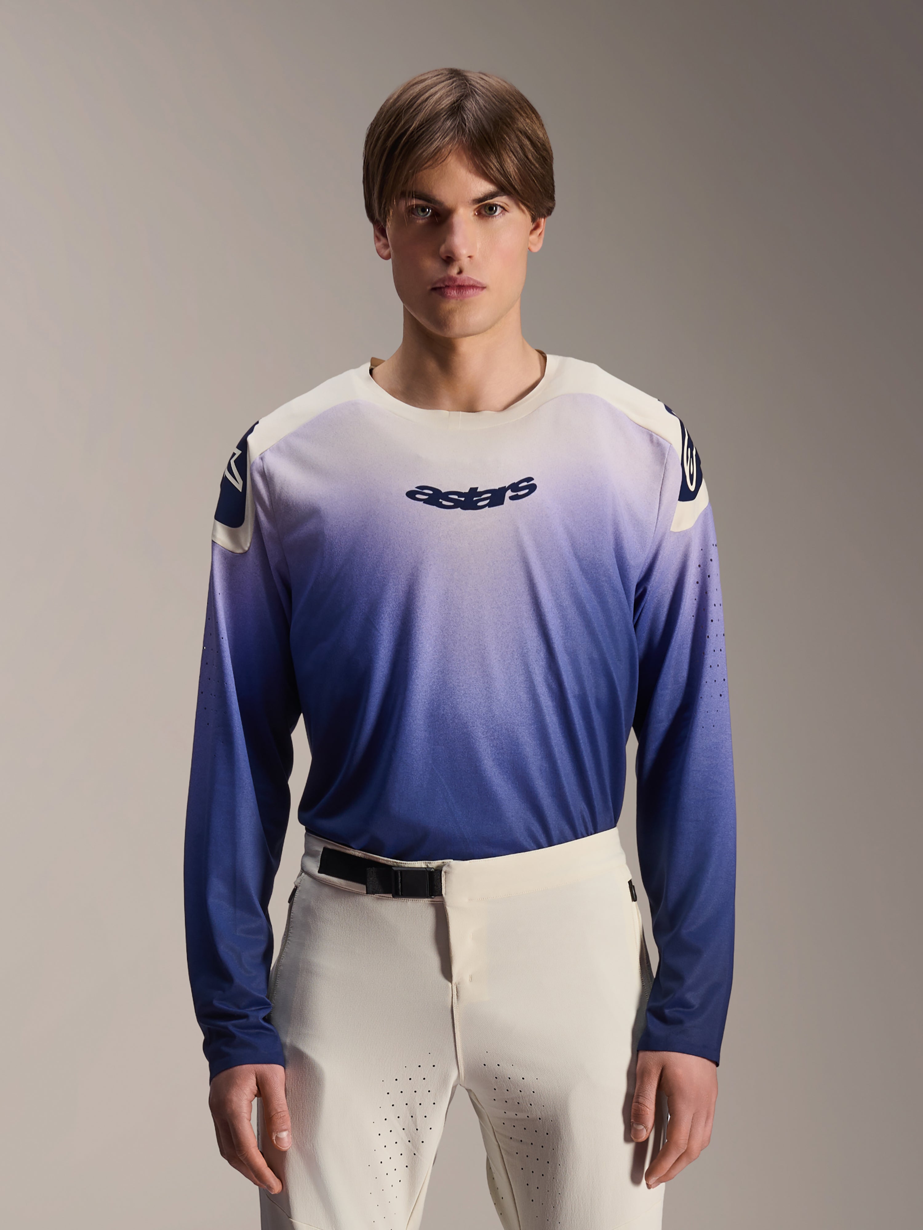 Alpinestars A-Aria Polartec Maker Elite Jersey, Long Sleeve MTB Jersey, Baja Blue with white-to-blue gradient, worn by a model with white pants, featuring dark blue chest logo and laser perforations on sleeves, performance mountain biking apparel