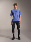 Alpinestars A-Aria Elite Shorts, MTB Mountainbike-Shorts, Black Titanium, getragen mit blauem Kurzarmtrikot, Knieschützern und schwarzen Bikeschuhen, Ganzkörper-Studioaufnahme, Performance-Mountainbike-Bekleidung