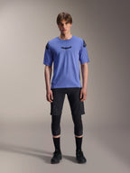 Alpinestars A-Aria Elite Shorts, MTB Mountainbike-Shorts, Black Titanium, getragen mit blauem Kurzarmtrikot, Knieschützern und schwarzen Bikeschuhen, Ganzkörper-Studioaufnahme, Performance-Mountainbike-Bekleidung