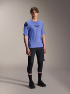 Männliches Model im Alpinestars A-Aria Polartec Elite Kurzarmtrikot in Baja Blue, kombiniert mit schwarzen MTB-Shorts und Knieschonern, mit schwarzen Astars-Logos auf der Brust und Schulter, hochwertige Performance-Mountainbike-Ausrüstung