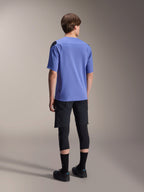 Alpinestars A-Aria Polartec Elite Kurzarmtrikot in Baja Blue, Rückansicht an einem männlichen Model, kombiniert mit schwarzen MTB-Shorts und Knieschutz, mit einer Performance-Passform und verlängertem Rückensaum für Trailfahrten.