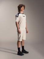 Alpinestars A-Aria Polartec Elite Kurzarmtrikot, Ecru mit schwarzen Schultereinsätzen und Logo, getragen von einem Model mit passenden Shorts und schwarzen Schuhen, Performance-Mountainbike-Bekleidung für Offroad-Trailfahrten.