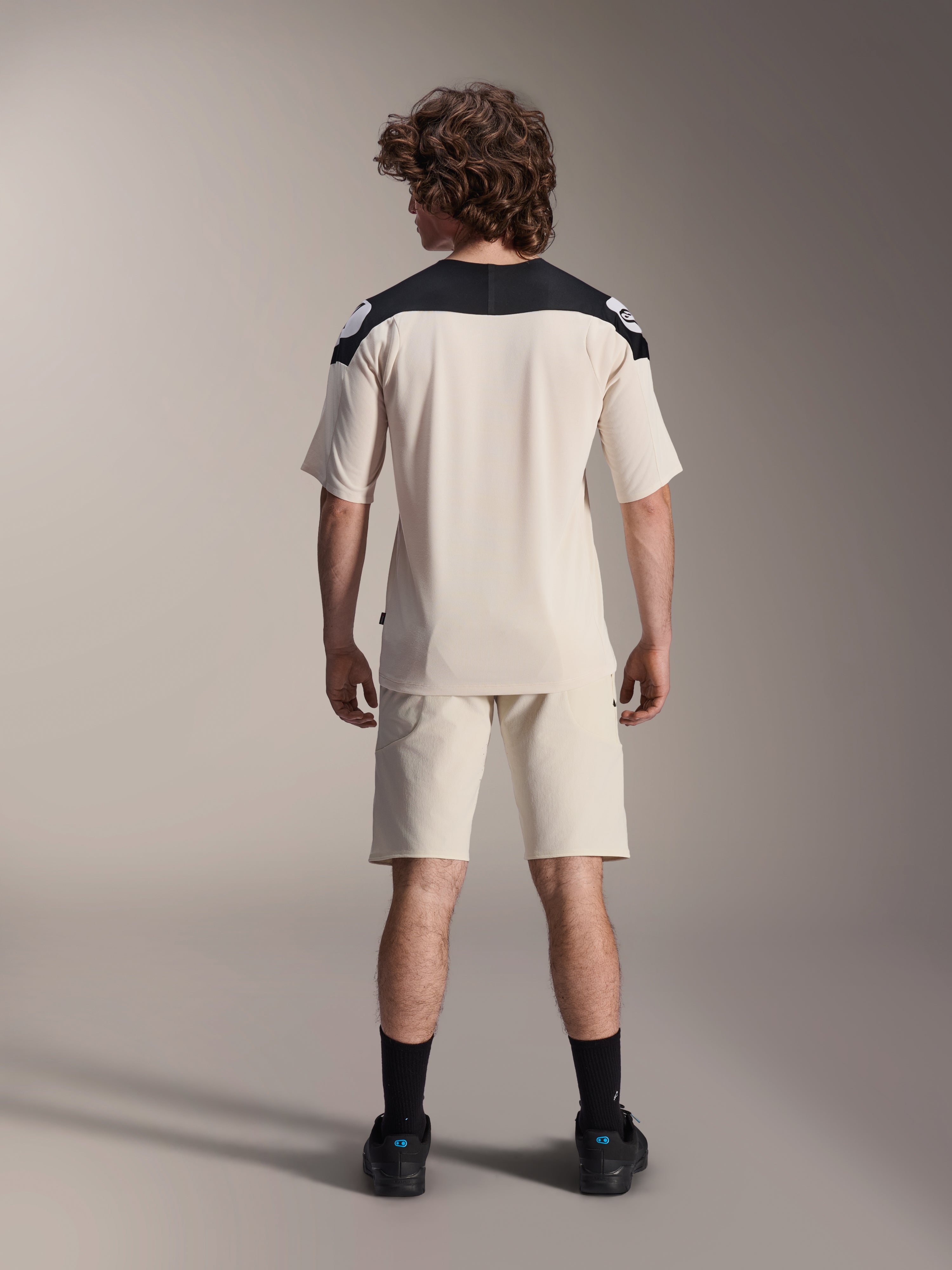 Alpinestars A-Aria Polartec Elite Kurzarmtrikot, MTB-Fahrradtrikot, Ecru mit schwarzen Schulterpartien, Rückansicht mit passenden Shorts und schwarzen Socken, Performance-Passform mit verlängertem Rückenteil für den Offroad-Einsatz.