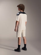 Modell trägt das Alpinestars A-Aria Polartec Elite Kurzarmtrikot in Ecru, Rückansicht, mit schwarzen Schulterpartien und weißem Logo, kombiniert mit passenden Mountainbike-Shorts in Ecru und schwarzen Schuhen