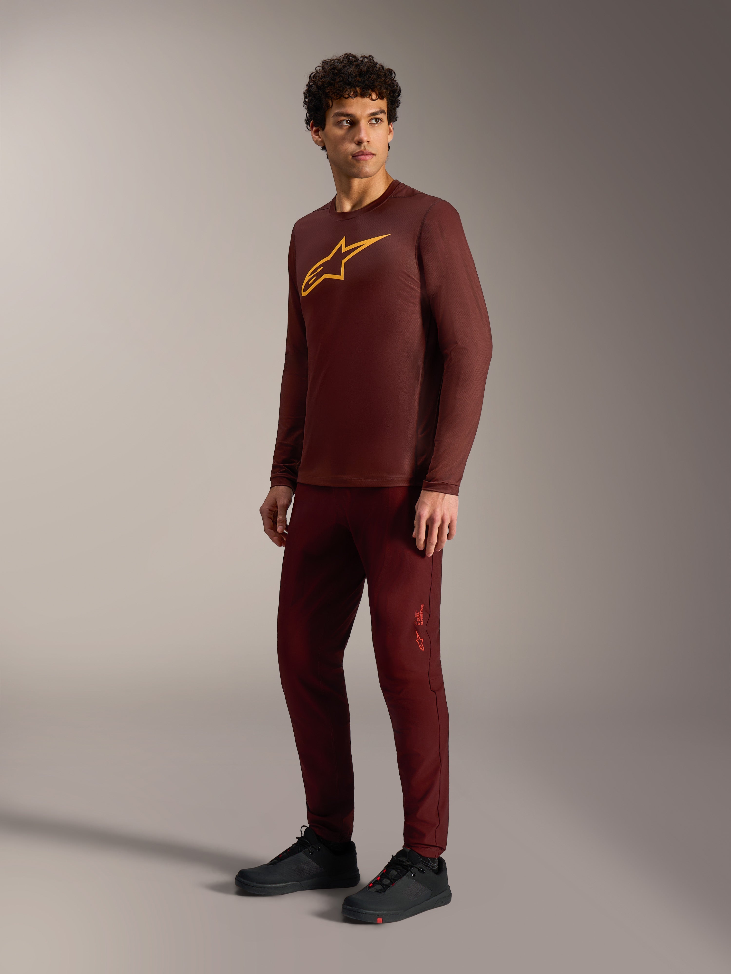 Bordeauxfarbenes A-Dura Ride Langarmtrikot mit gelbem Astars-Logo, passender Hose und schwarzen MTB-Schuhen.
