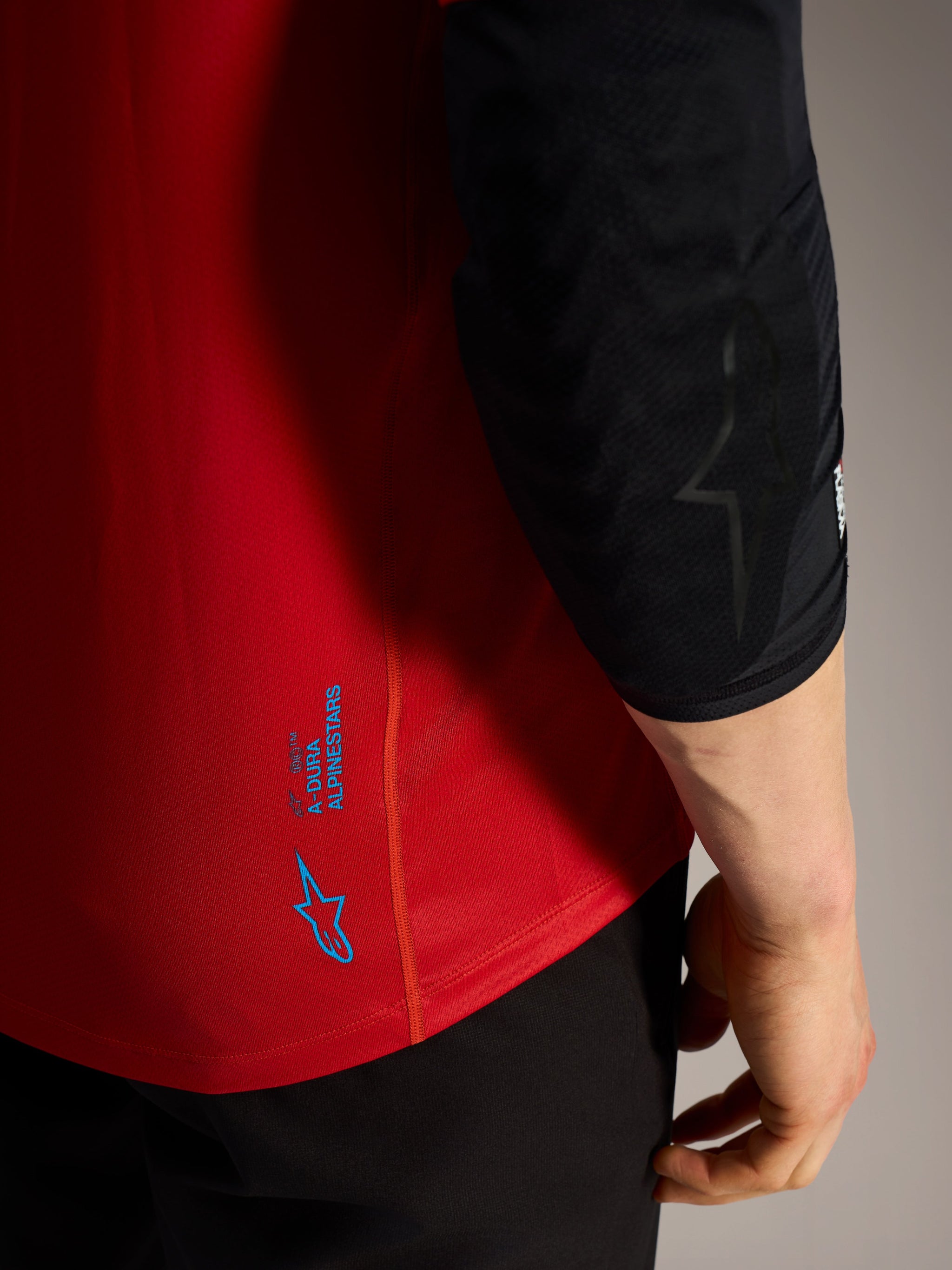 Rotes Alpinestars A-Dura Ride Kurzarmtrikot, Detailansicht mit blauen Logos und technischem MTB-Funktionsstoff.
