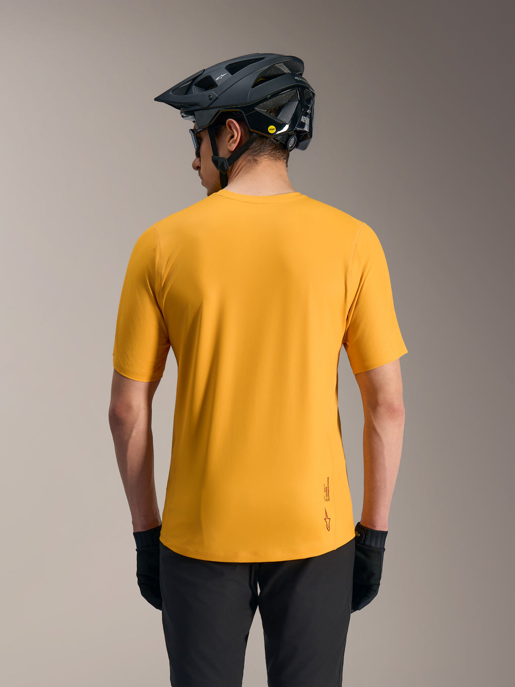 Oranges A-Dura Ride Kurzarmtrikot, leichtes MTB-Oberteil mit Logo und verlängertem Rücken, Rückansicht mit Helm.