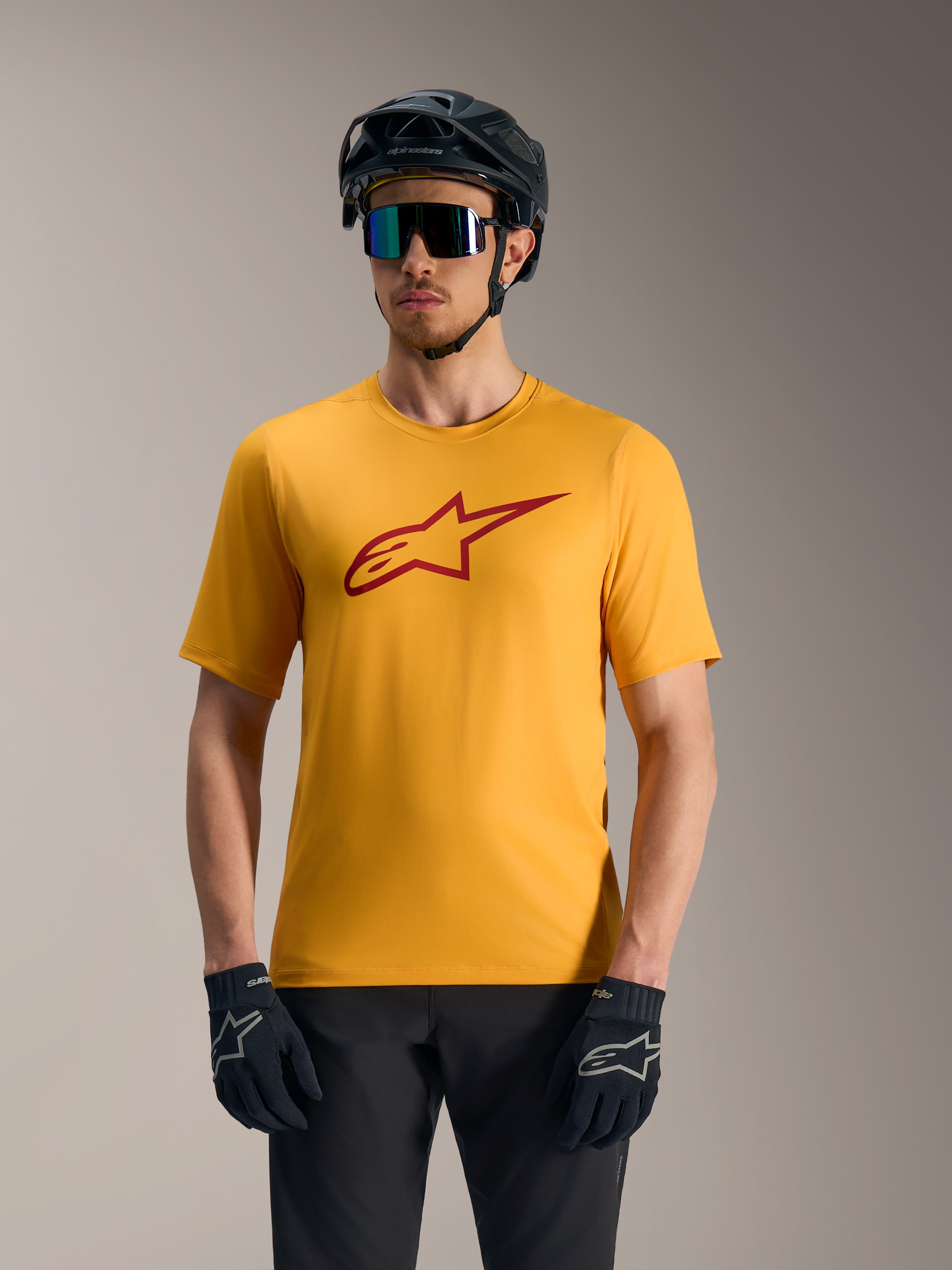 Oranges A-Dura Ride Kurzarmtrikot mit rotem Astars-Logo, kombiniert mit MTB-Helm und Handschuhen.