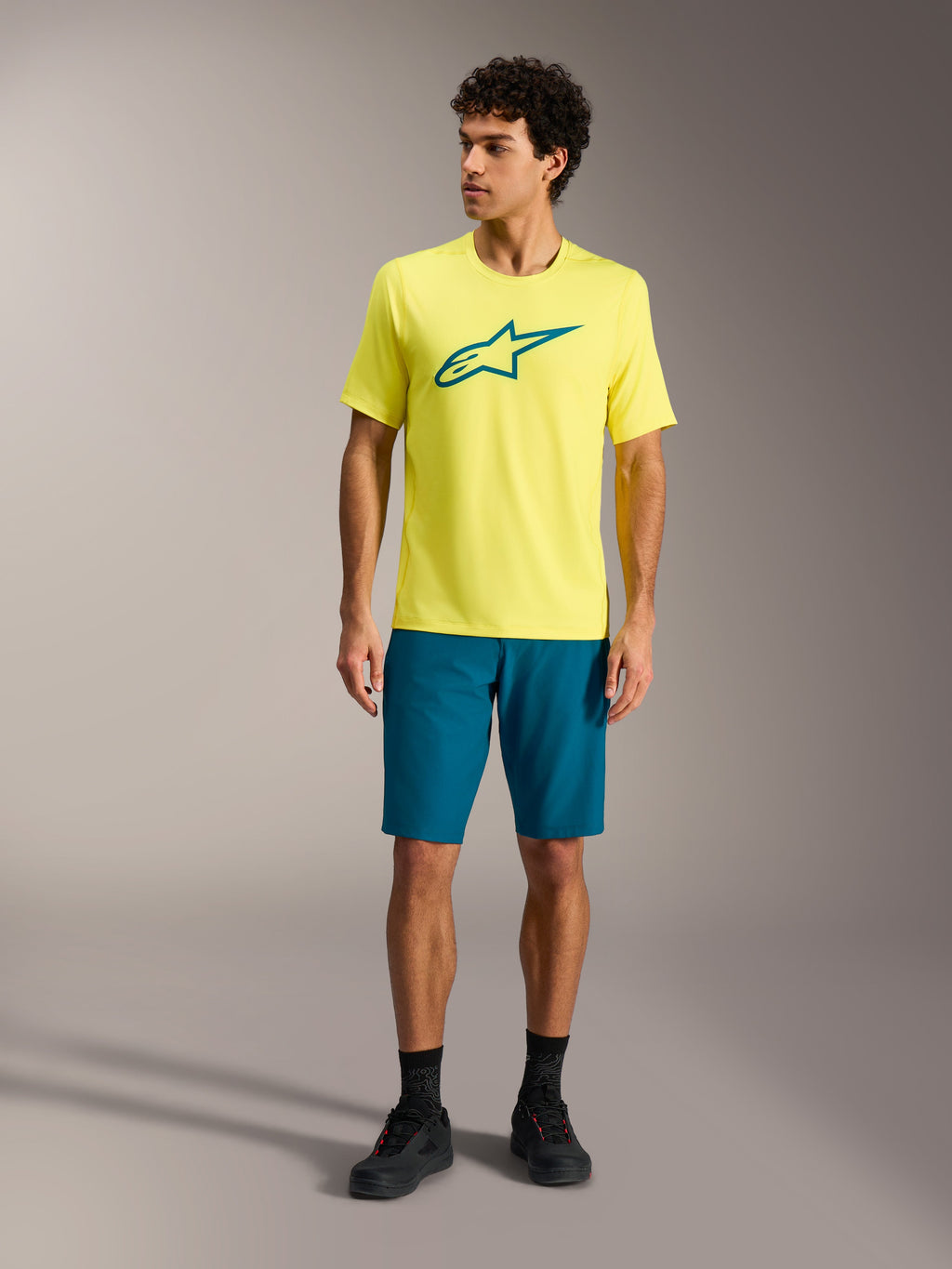 Gelbes Alpinestars A-Dura Ride SS Jersey und blaugrüne Shorts, Mountainbike-Performance-Outfit im Studio.