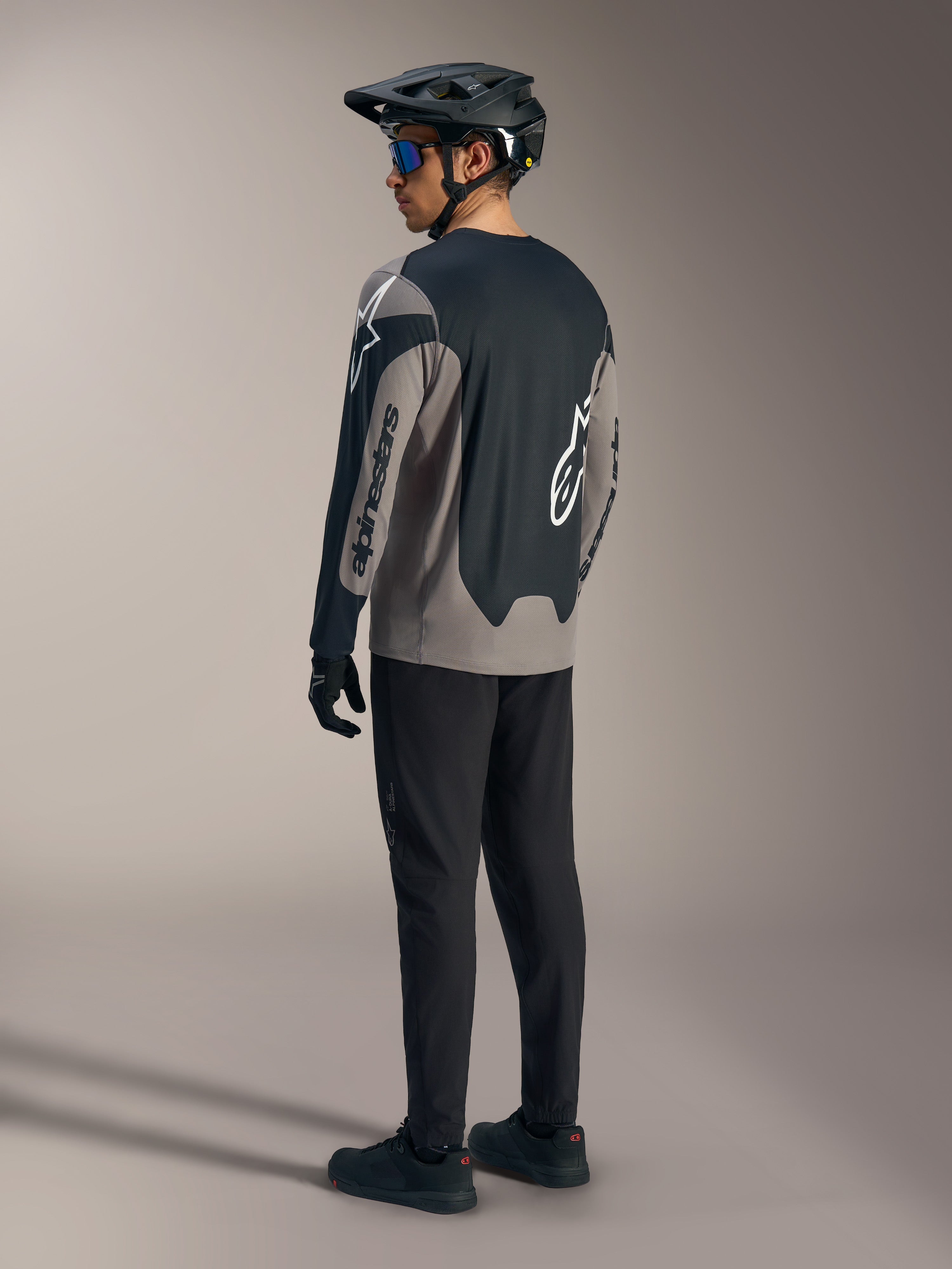 Grau-schwarzes A-Dura Race Langarmtrikot von Alpinestars, Rückansicht in kompletter Mountainbike-Ausrüstung.