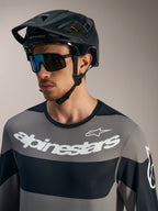 Graues Alpinestars A-Dura Race Langarmtrikot mit weißen Logos, schwarzem MTB-Helm und Performance-Sonnenbrille.