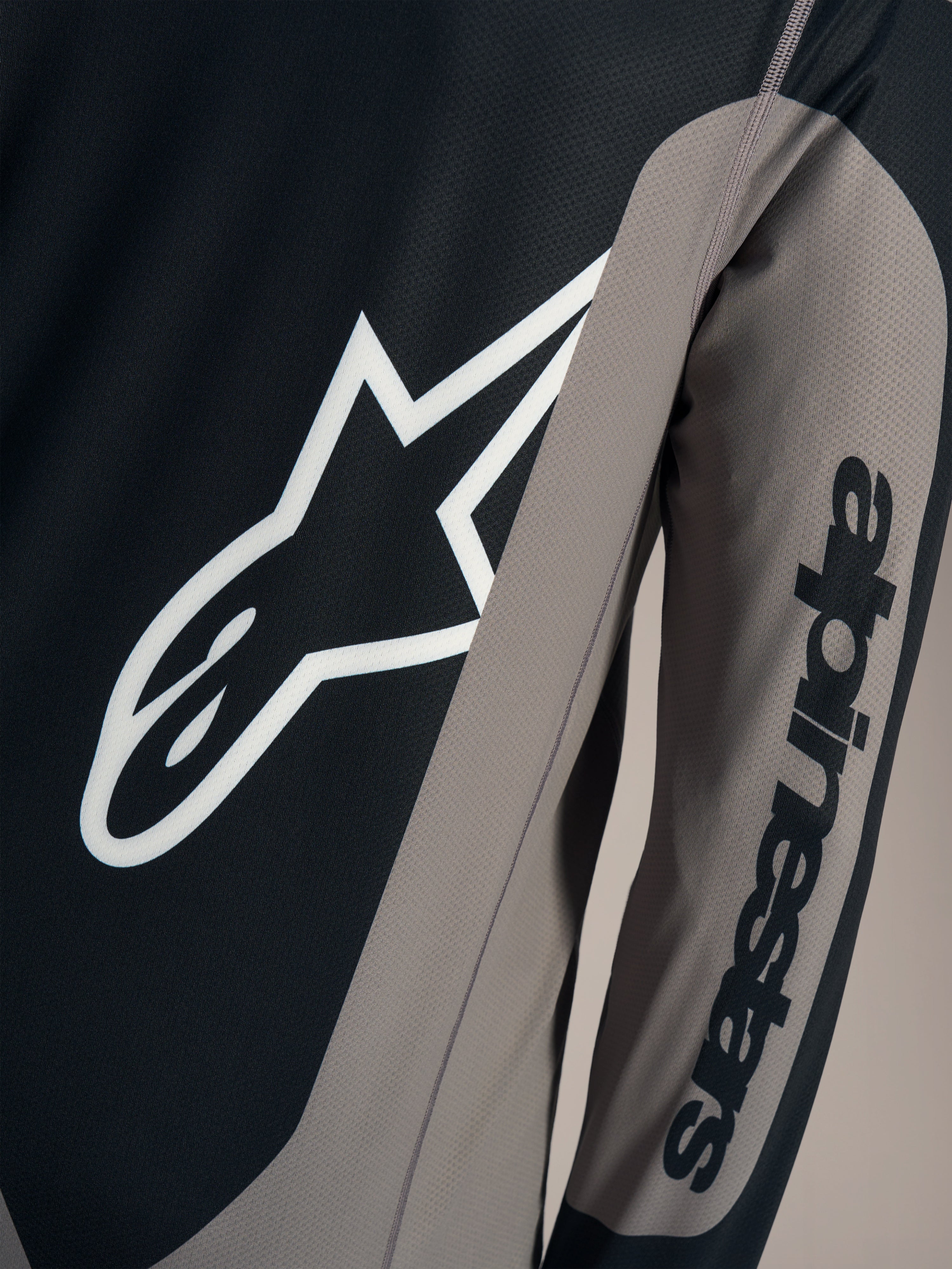 Graues A-Dura Race Langarmtrikot, Detail mit weißem Astars-Logo und Alpinestars-Schriftzug am Ärmel.