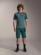 Alpinestars A-Dura Lipan Trikot, Kurzarm-MTB-Trikot, Silver Pine Grün mit schwarz-orangem Astars-Logo auf der Brust, kombiniert mit passenden Shorts und schwarzem Schuhwerk, technische Mountainbike-Bekleidung