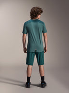 Alpinestars A-Dura Lipan Kurzarmtrikot in Silver Pine, Rückansicht mit texturierten Jacquard-Schulterbahnen und verlängertem Drop-Tail-Saum, getragen mit passenden dunkelgrünen Mountainbike-Shorts und schwarzen Schuhen.