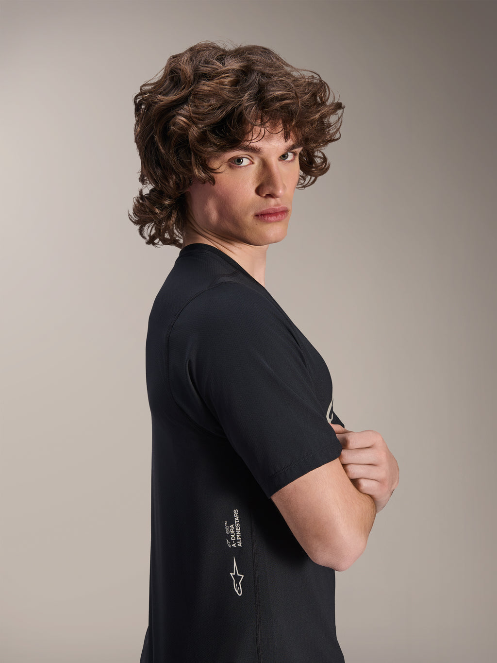 Alpinestars A-Dura Astar Jersey, Short Sleeve MTB Jersey, Black, male model posing in profile with arms crossed, featuring white Alpinestars branding on the lower side, casual athletic design for mountain biking.