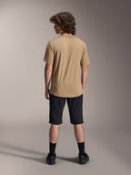 Männliches Model von hinten in schwarzen Alpinestars A-Dura Shorts und einem hellbraunen A-Dura Kurzarmtrikot, kombiniert mit schwarzen Socken und Mountainbikeschuhen, funktionales MTB-Trail-Outfit