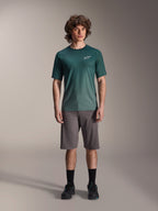 Männliches Model trägt Alpinestars A-Dura Rise Kurzarmtrikot in Silver Pine, grünes Radsporttrikot mit kleinem weißem Brustlogo, kombiniert mit grauen Mountainbike-Shorts und schwarzem Schuhwerk, lässige MTB-Trail-Ausrüstung