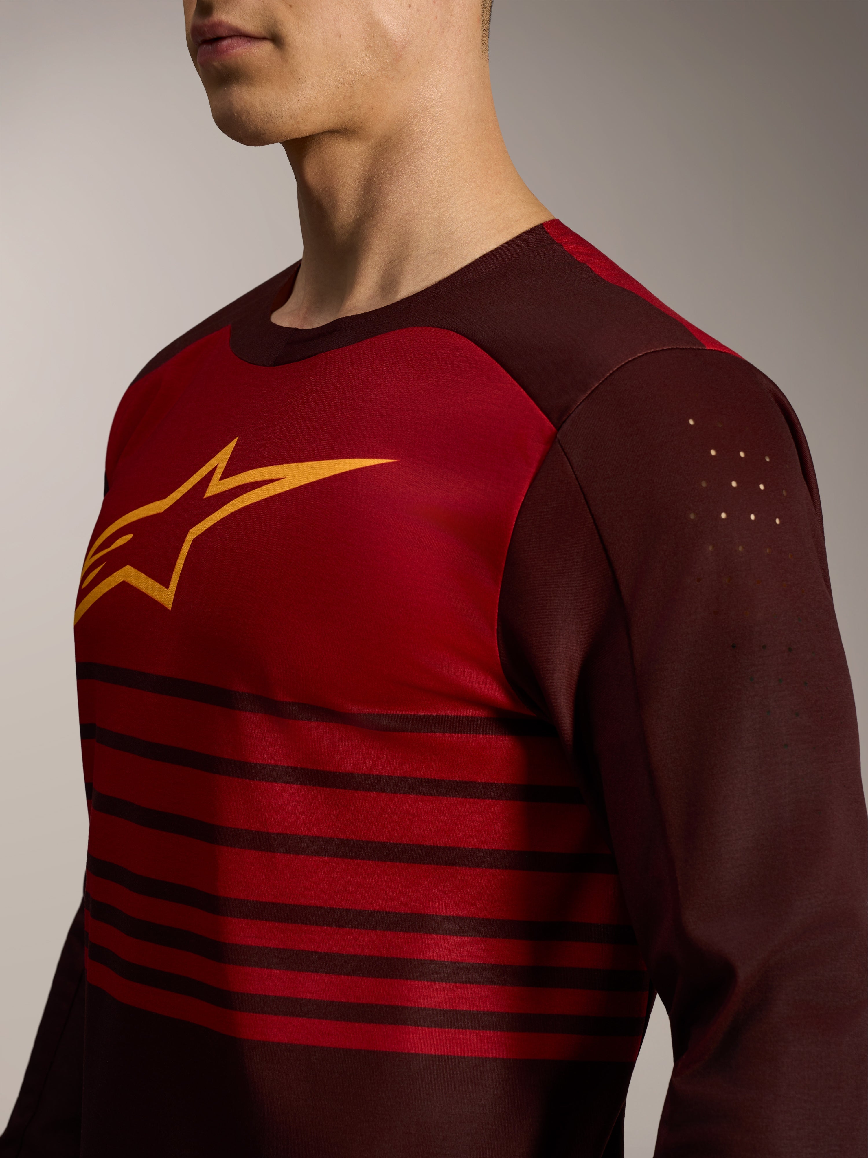 A-Dura Elite Langarmtrikot 2.0 in Bordeauxrot mit gelbem Brustlogo und lasergeschnittenen Bizeps-Perforationen.