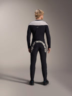 Mann in der Rückansicht trägt das Alpinestars A-Supra Melt Langarm-Trikot in Schwarz, hellgrauer Schultereinsatz, kombiniert mit einer schwarzen MTB-Hose mit großem Alpinestars-Logo auf dem Gesäß, Performance-Mountainbike-Ausrüstung.