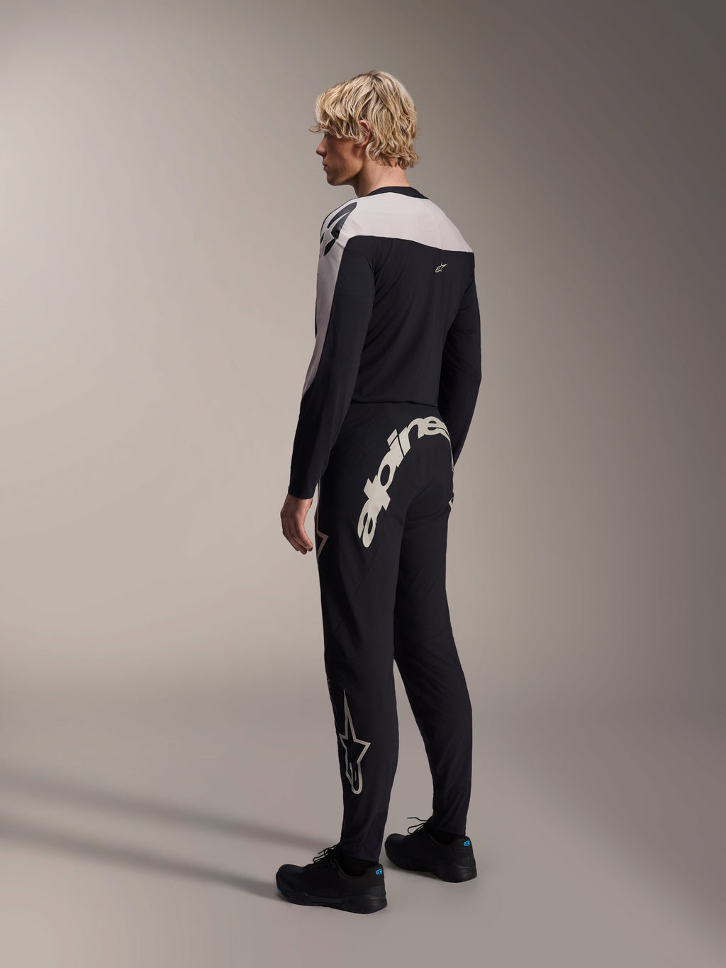 Alpinestars A-Supra Melt Hose, MTB-Hose, Schwarz, mit einem großen weißen Alpinestars-Schriftzug auf der Rückseite und Stern-Logo am Bein, getragen von einem Modell mit einem passenden langärmeligen Trikot und schwarzen Schuhen, Rückansicht
