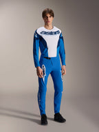 Model in kompletter Alpinestars MTB-Rennausrüstung, blau-weißes Langarmtrikot mit 'astars'-Branding, passende blaue A-Supra Melt Hose mit weißen Stern-Logos, professionelle Mountainbike-Bekleidung für das Gelände