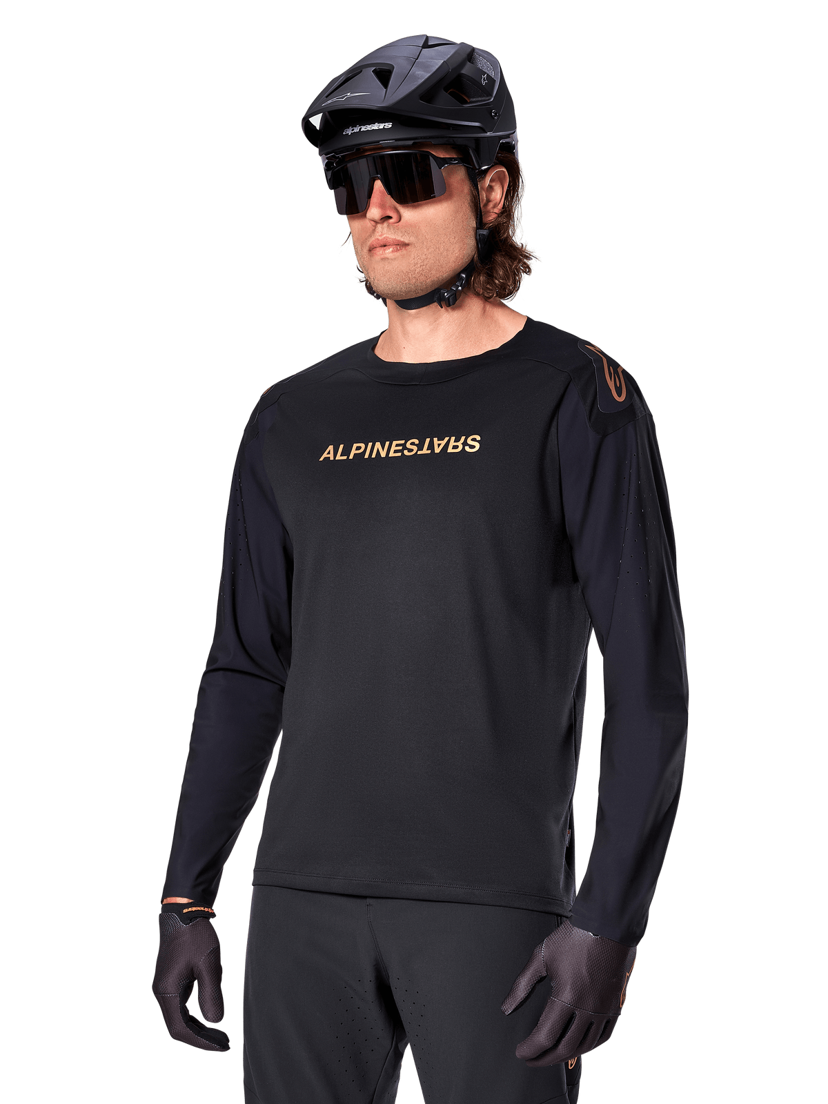 Alpinestars A-Aria Polartec Switch Langarmtrikot, Schwarz mit goldfarbenem Logo, MTB-Mountainbike-Bekleidung, getragen mit schwarzem Helm und Sonnenbrille, mit lasergeschnittenen Belüftungsöffnungen an den Ärmeln und feuchtigkeitsableitendem Polartec-Gewebe für Offroad-Performance