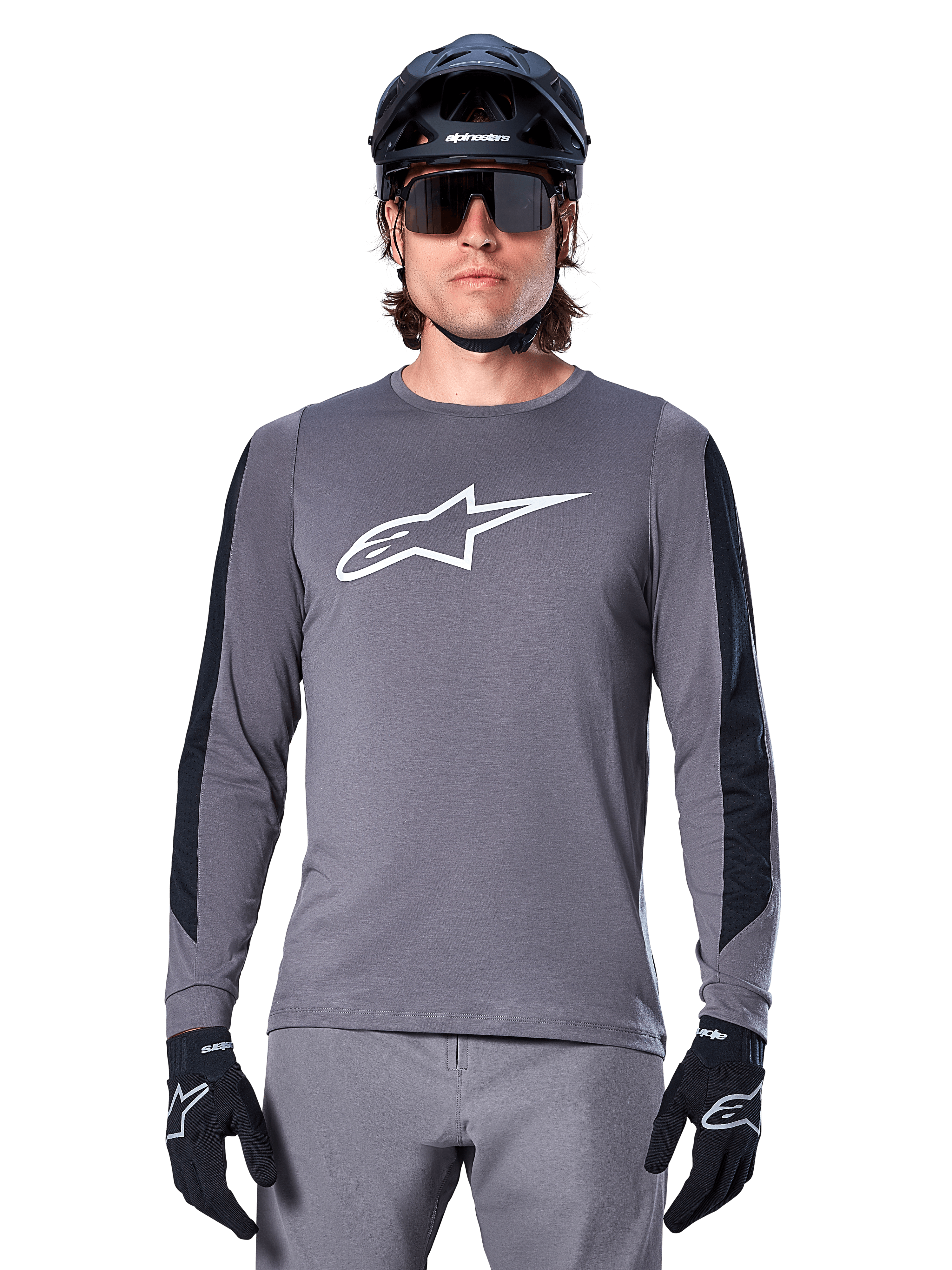 Alpinestars A-Dura Dri Astar Langarmtrikot, Dunkelgrau, mit großem weißen Astar-Logo auf der Brust und schwarzen Mesh-Einsätzen an den Armen, getragen von einem Fahrer mit schwarzem Mountainbike-Helm und Performance-Sonnenbrille, MTB-Radsportbekleidung