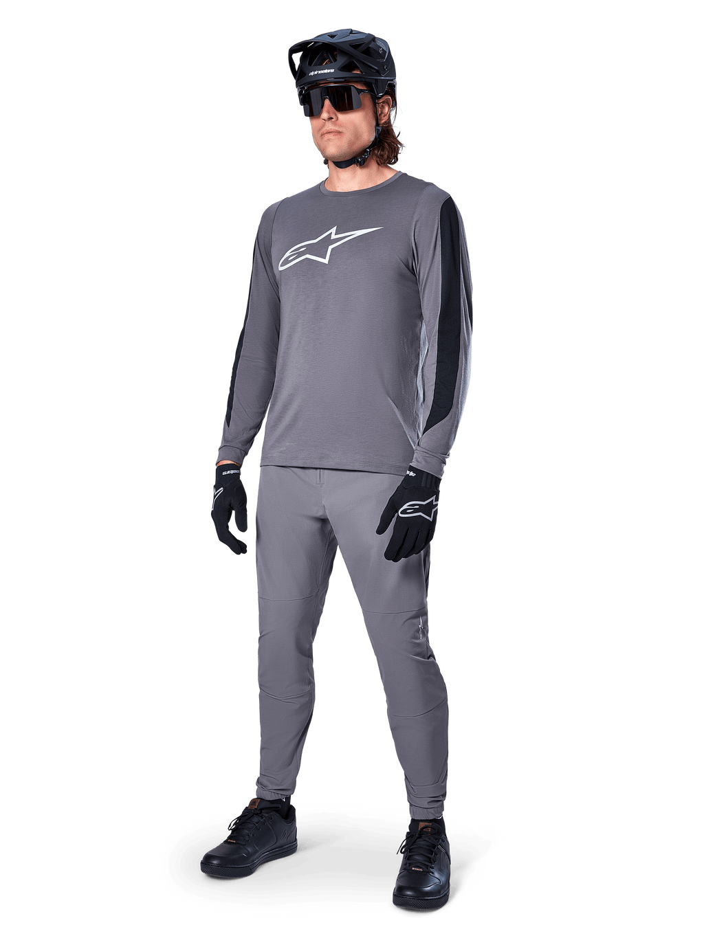Alpinestars A-Dura Dri Astar Langarm-MTB-Trikot, Dunkelgrau mit weißem Brustlogo, schwarze Mesh-Einsätze an den Ärmeln, kombiniert mit passender grauer Hose, schwarzem Helm und Handschuhen, Performance-Mountainbike-Bekleidung