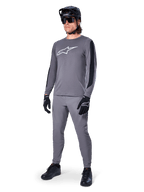 Alpinestars A-Dura Dri Astar Langarm-MTB-Trikot, Dunkelgrau mit weißem Brustlogo, schwarze Mesh-Einsätze an den Ärmeln, kombiniert mit passender grauer Hose, schwarzem Helm und Handschuhen, Performance-Mountainbike-Bekleidung