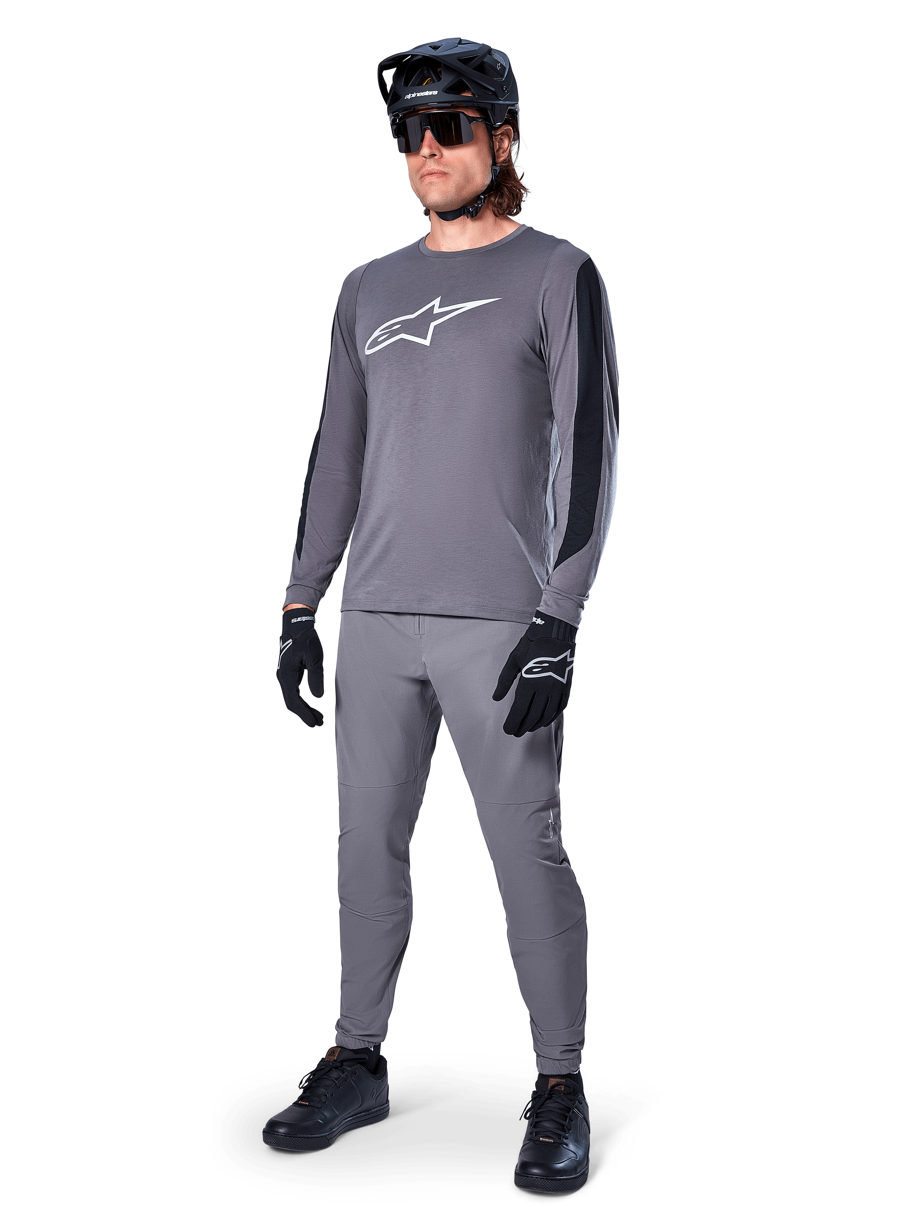 Alpinestars A-Dura Dri Astar Langarm-MTB-Trikot, Dunkelgrau mit weißem Brustlogo, schwarze Mesh-Einsätze an den Ärmeln, kombiniert mit passender grauer Hose, schwarzem Helm und Handschuhen, Performance-Mountainbike-Bekleidung
