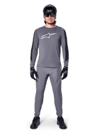 Alpinestars A-Dura Dri Astar Jersey, langärmeliges MTB-Trikot in Dunkelgrau, mit weißem Brustlogo und schwarzen Ärmeleinsätzen, getragen mit passender grauer Hose, schwarzem Helm, Sonnenbrille und Handschuhen für ein komplettes Offroad-Radsport-Outfit