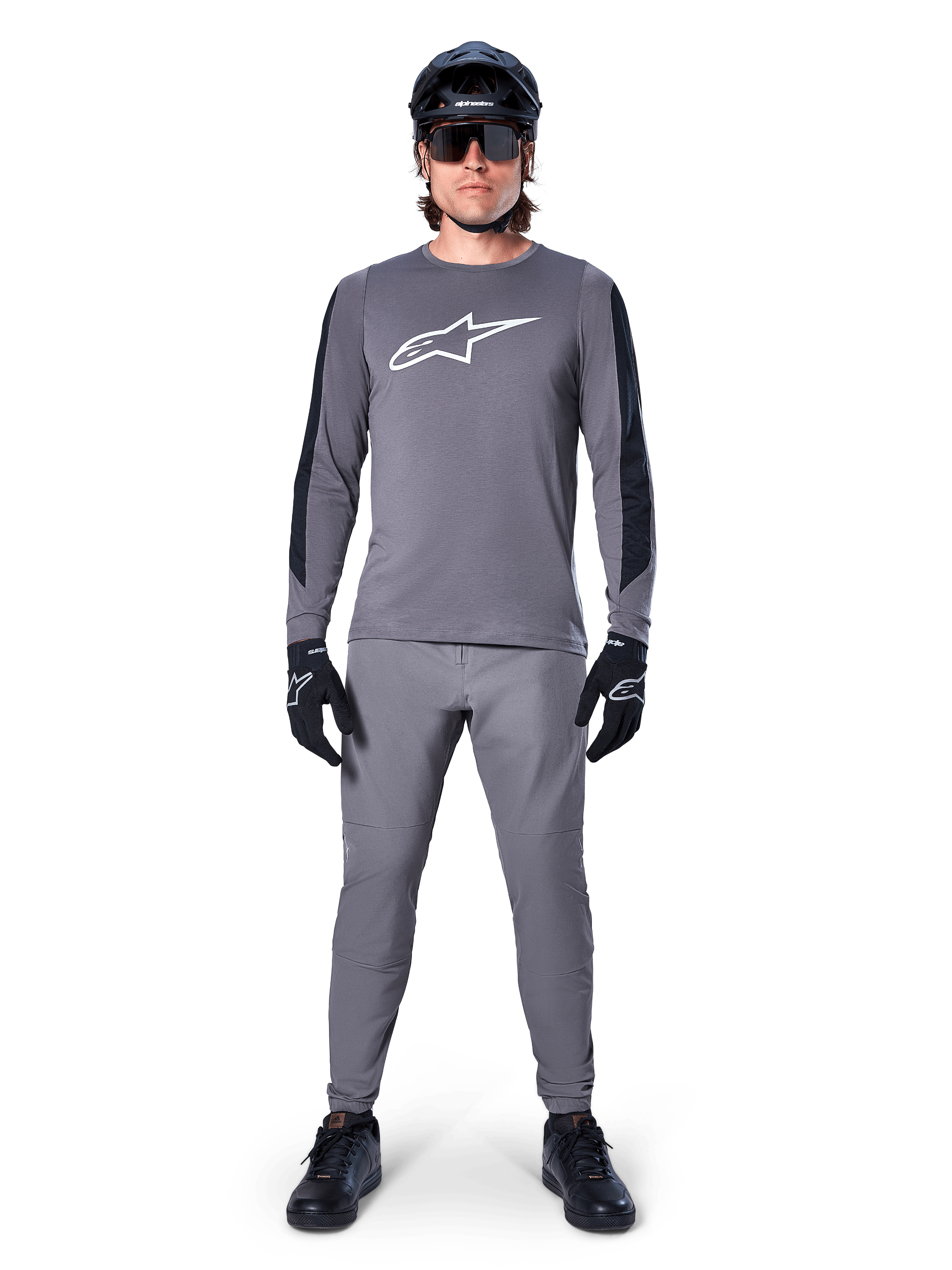 Alpinestars A-Dura Dri Astar Jersey, langärmeliges MTB-Trikot in Dunkelgrau, mit weißem Brustlogo und schwarzen Ärmeleinsätzen, getragen mit passender grauer Hose, schwarzem Helm, Sonnenbrille und Handschuhen für ein komplettes Offroad-Radsport-Outfit