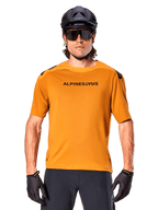 Alpinestars A-Aria Polartec Switch Kurzarm-Trikot, Dunkelgold, Mountainbike-Fahrer mit schwarzem Helm und Sonnenbrille, Performance-Radsportbekleidung für MTB-Trails