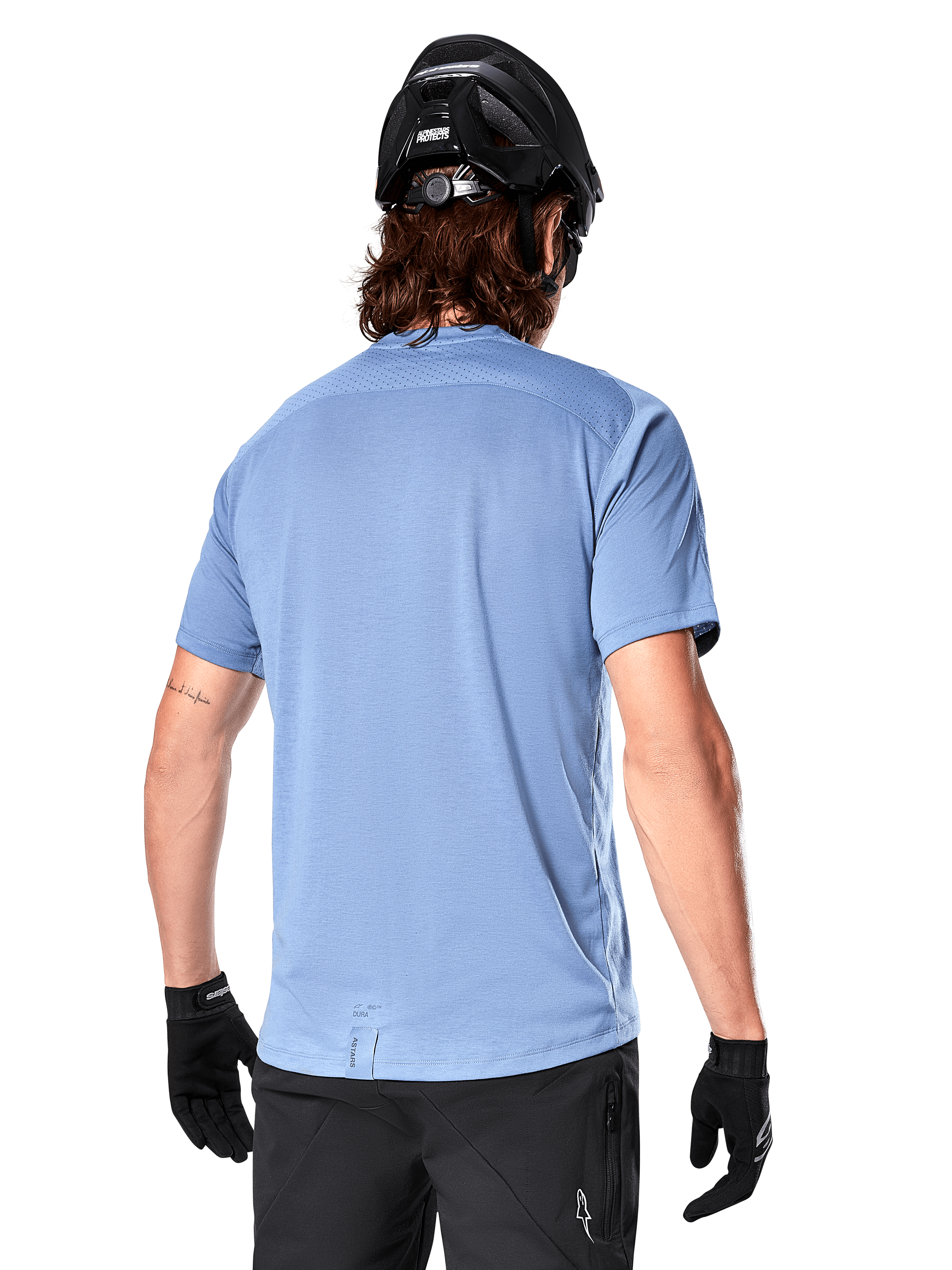 Alpinestars A-Dura Dri Astar Kurzarmtrikot, MTB-Trikot, Infinity Blue, Rückansicht mit Mesh-Belüftungseinsätzen an den Schultern und verlängertem Rücken, kombiniert mit schwarzem MTB-Helm und Handschuhen, Performance-Radbekleidung