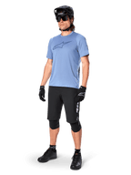 Männlicher Fahrer im Alpinestars A-Dura Dri Astar Kurzarmtrikot in Infinity Blue, kombiniert mit schwarzen MTB-Shorts, schwarzem Helm, Sonnenbrille, Knieschützern und Handschuhen, komplettes Mountainbike-Outfit