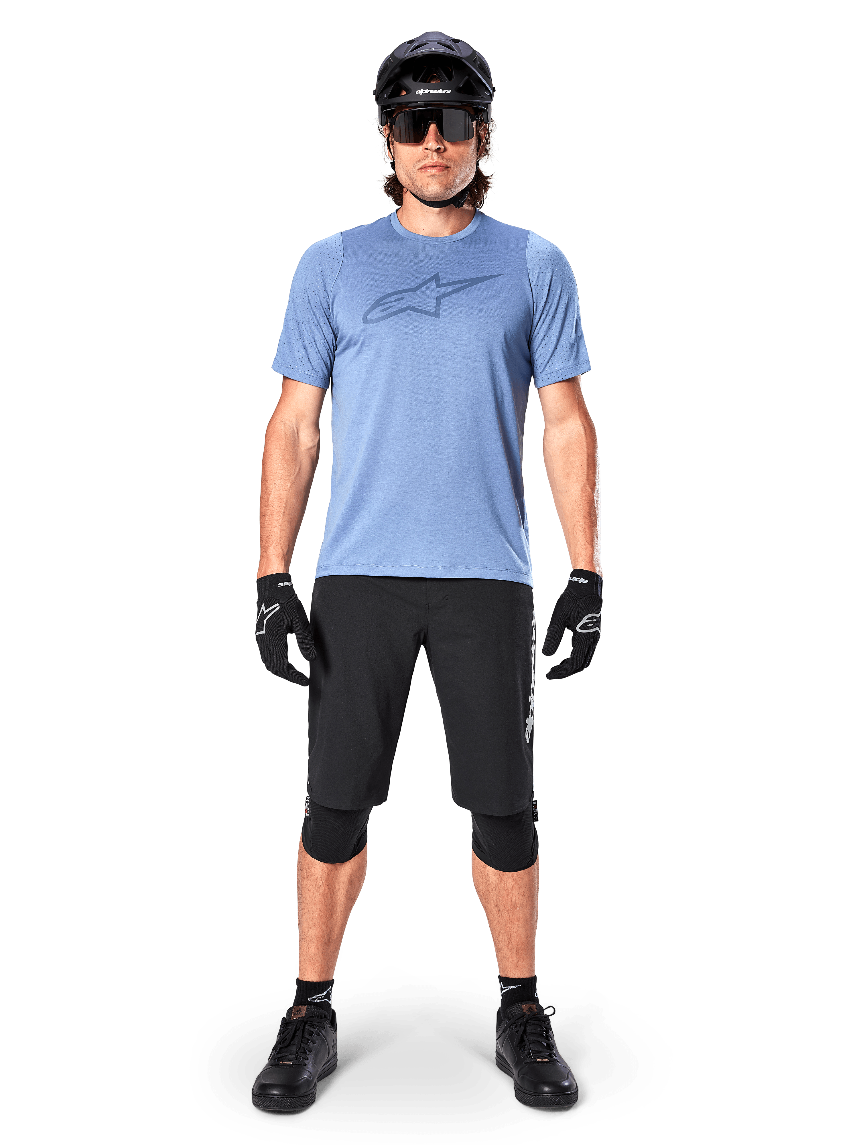 Männlicher Mountainbike-Fahrer im Alpinestars A-Dura Dri Astar Kurzarmtrikot in Infinity Blue, mit markantem Astars-Logo auf der Brust, kombiniert mit schwarzen MTB-Shorts, schwarzem Helm, Sonnenbrille und Schutzausrüstung für Geländefahrten