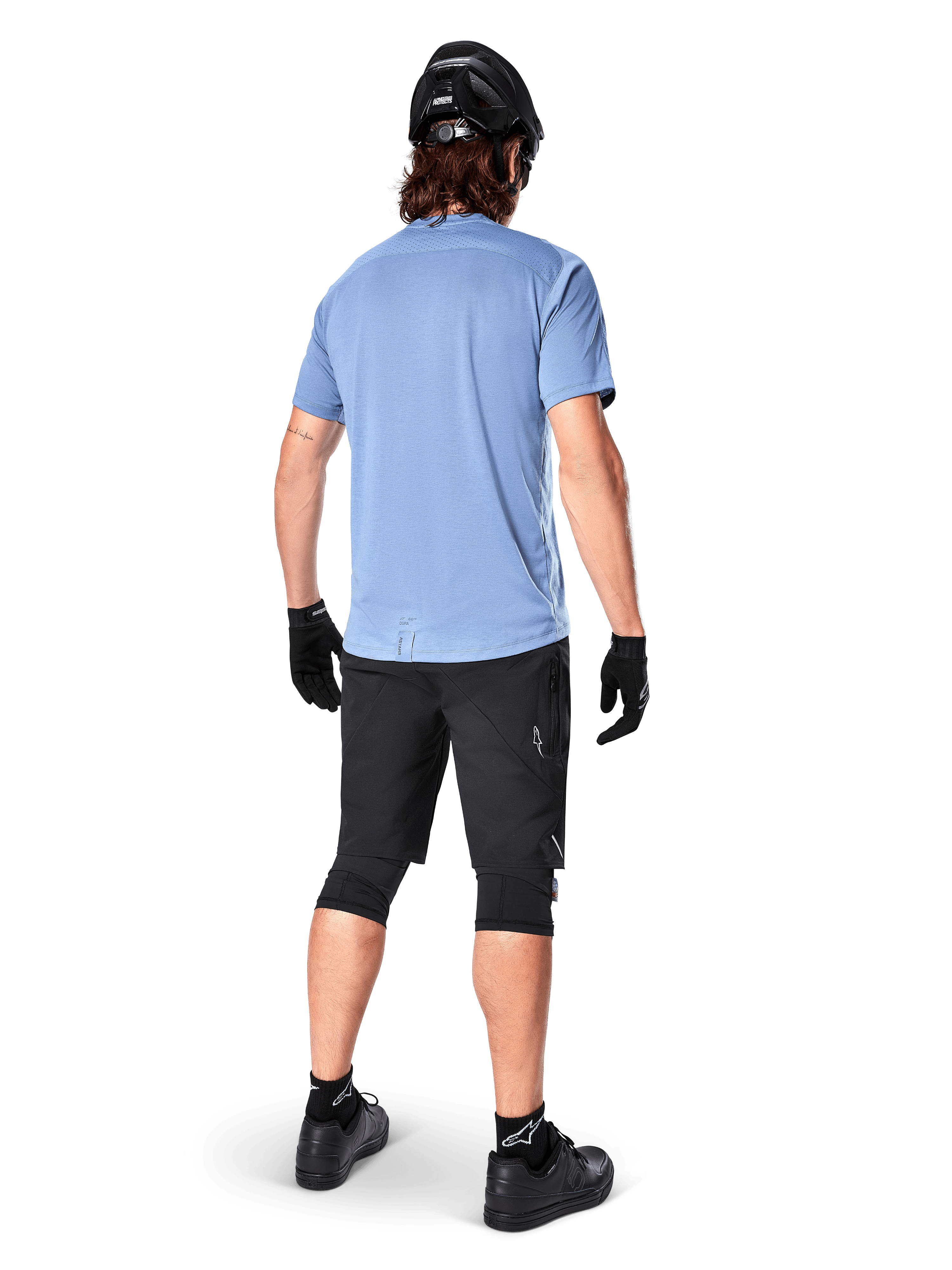 Alpinestars A-Dura Dri Astar Kurzarmtrikot, Infinity Blue, Rückansicht, kombiniert mit schwarzen Mountainbike-Shorts und Helm, technische Radsportbekleidung mit feuchtigkeitsableitendem Material und verlängertem Rückenteil