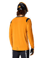 Alpinestars A-Dura Dri Wool Langarmtrikot in Dark Gold, Rückansicht eines Fahrers mit Mountainbike-Helm und Handschuhen, verfügt über schwarze Mesh-Einsätze an den Schultern und ein verlängertes Rückenteil, technische Radsportbekleidung für Trailfahrten