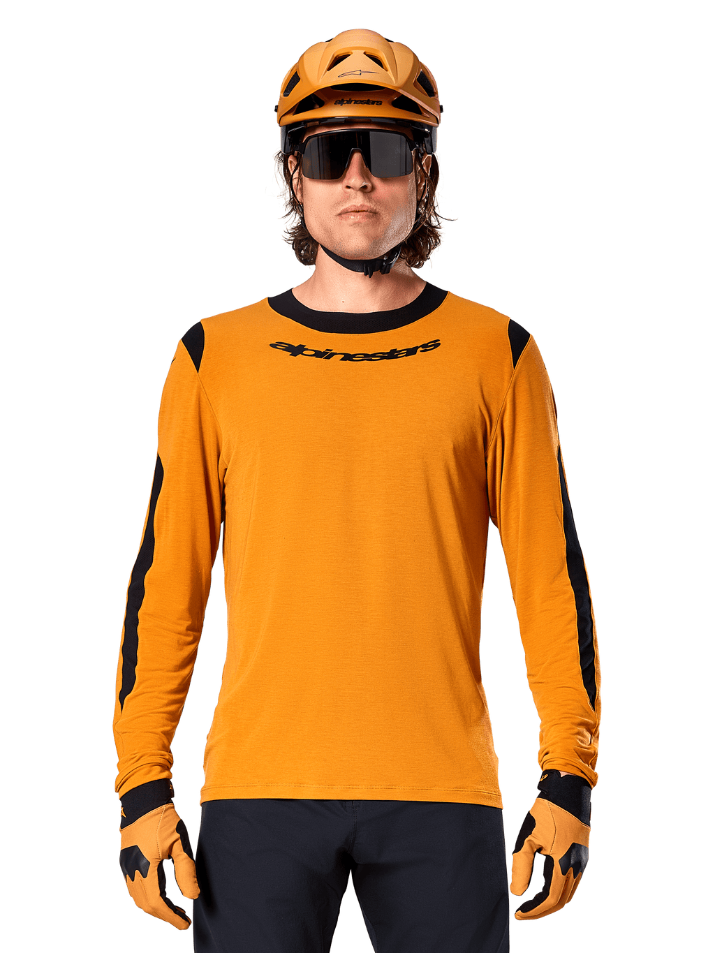 Männliches Model im Alpinestars A-Dura Dri Wool Langarmtrikot in Dark Gold, kombiniert mit einem passenden goldenen MTB-Helm und Handschuhen, schwarze Mesh-Einsätze an Schultern und Ärmeln, schwarzer Alpinestars-Schriftzug auf der Brust, dunkle Sonnenbrille und Hose, technische Mountainbike-Bekleidung