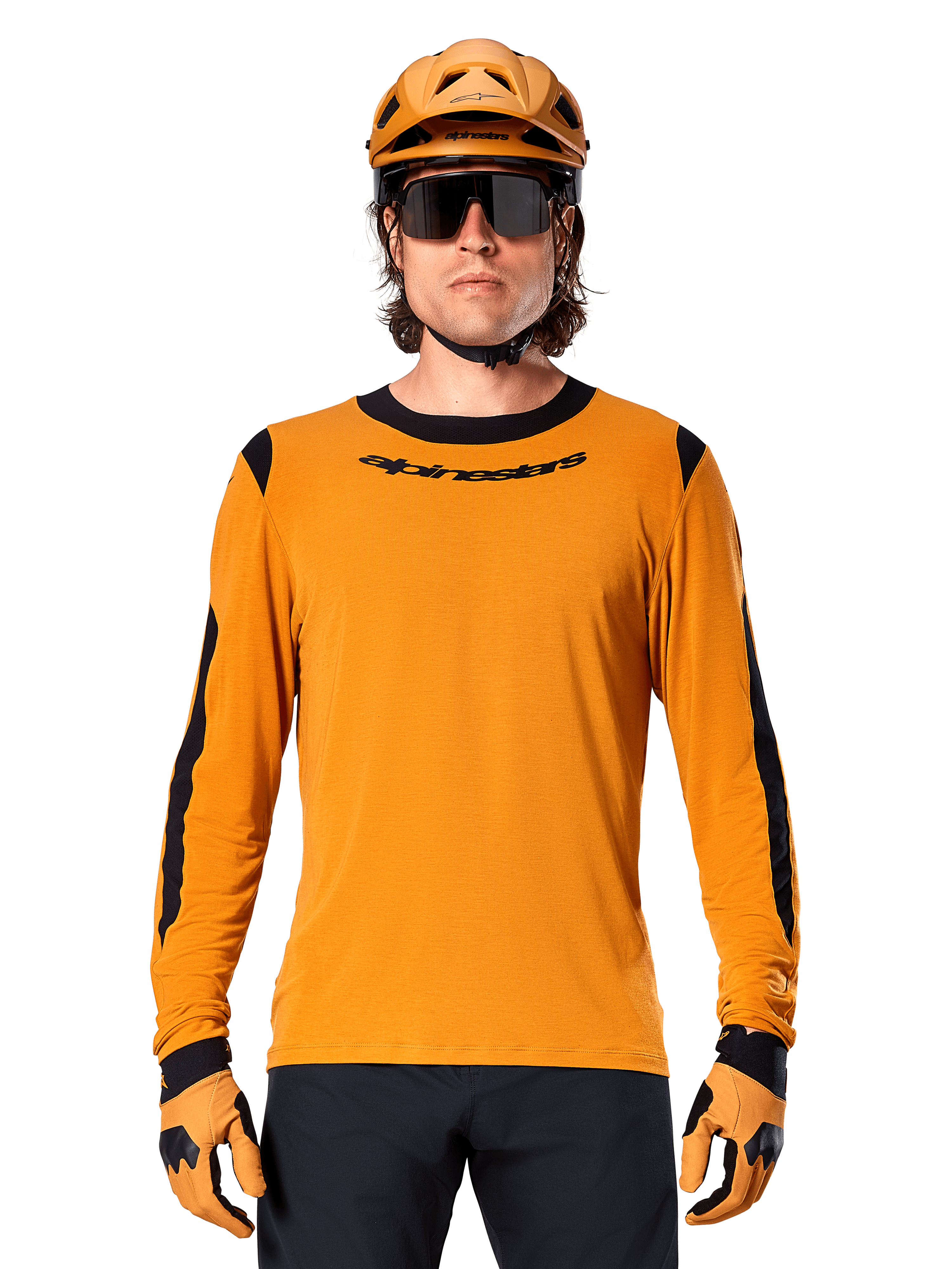 Männliches Model im Alpinestars A-Dura Dri Wool Langarmtrikot in Dark Gold, kombiniert mit einem passenden goldenen MTB-Helm und Handschuhen, schwarze Mesh-Einsätze an Schultern und Ärmeln, schwarzer Alpinestars-Schriftzug auf der Brust, dunkle Sonnenbrille und Hose, technische Mountainbike-Bekleidung