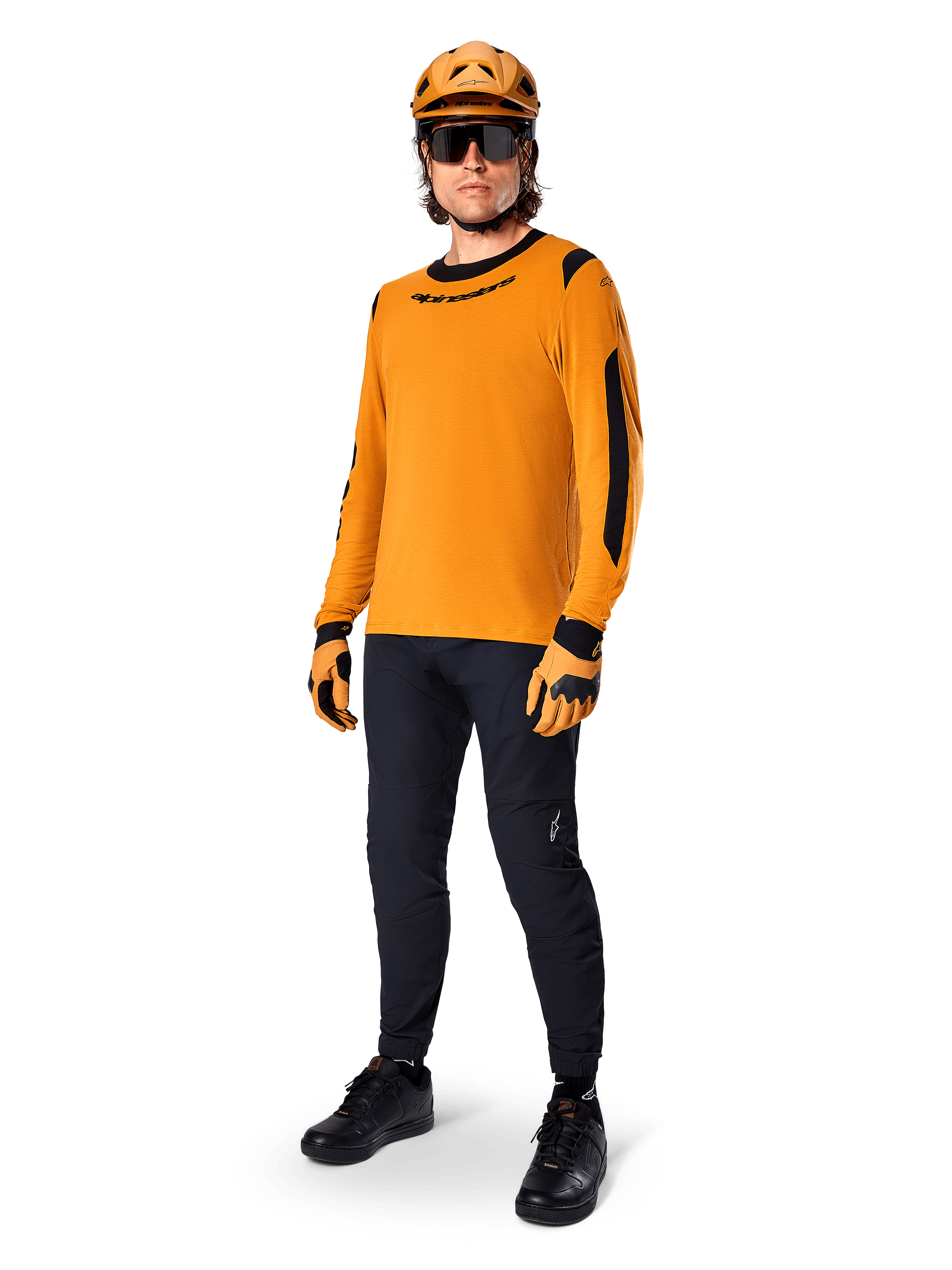 Alpinestars A-Dura Dri Wool Langarmtrikot, Dark Gold, getragen mit passendem orangefarbenem Helm, schwarzer MTB-Hose und gelb-schwarzen Handschuhen, komplettes Radsport-Outfit für Offroad-Trailfahrten